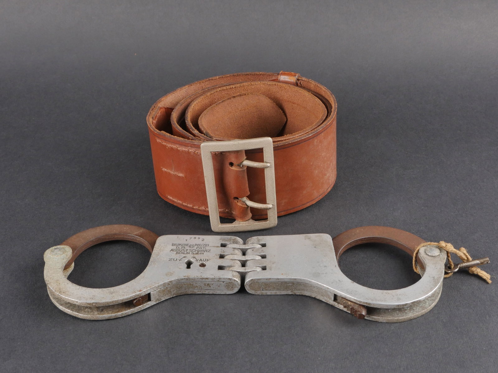 Accessoires Polizei. Polizei Accessories.: Accessoires de la Polizei comprenant un ceinturon d’officier en cuir marron, passants en cuir presents, boucle a ardillon en metal grenele, fabrication L&F, ainsi qu’une paire de menottes complete