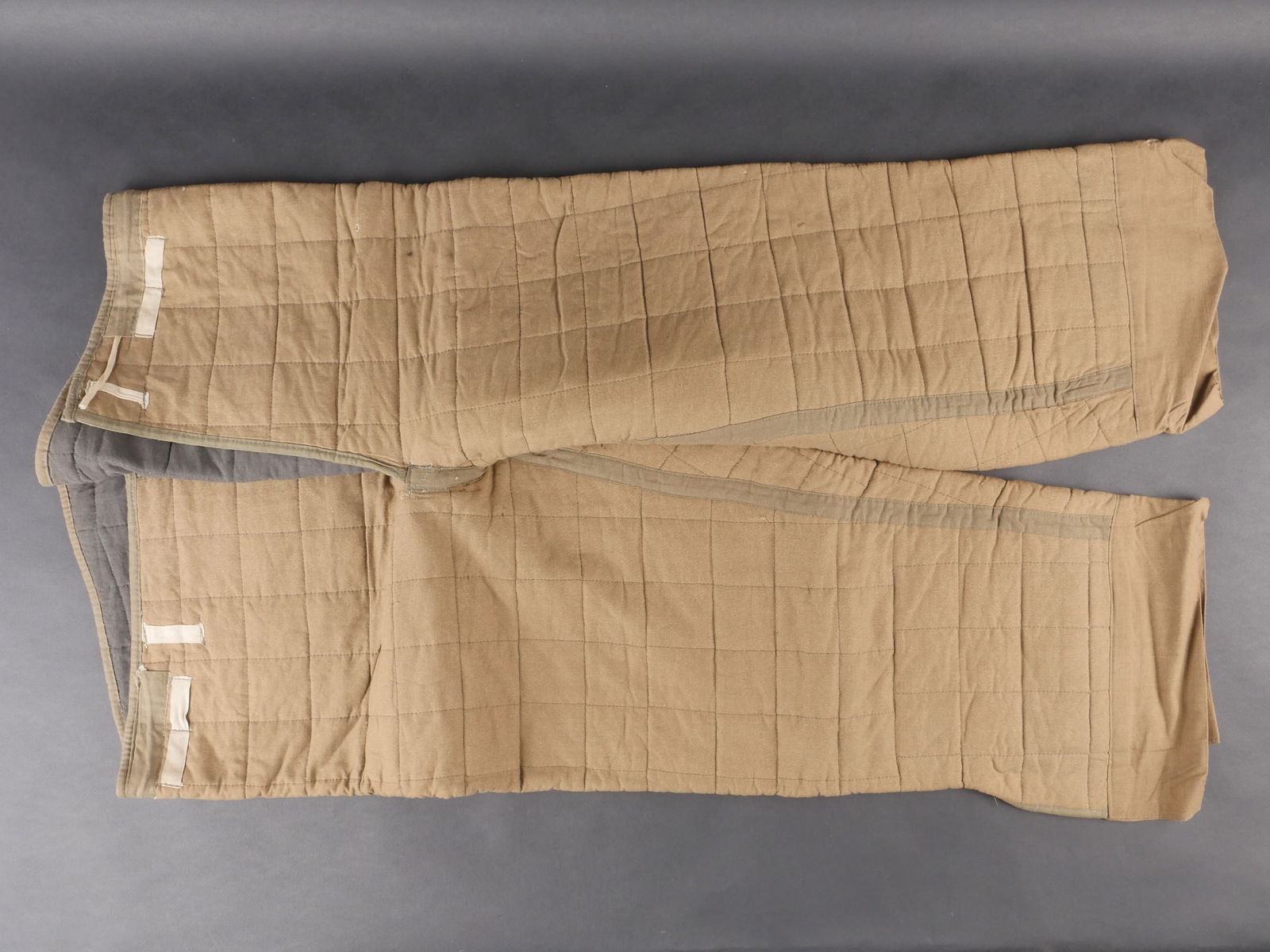 Sous-pantalon matelasse. Quilted undertrousers: Sous-pantalon matelasse en tissu marron, interieur double de coton noir. Cordons de serrage incomplets. Marquages absents. Presente une usure significative, patine homogene et taches visibles. Etat II