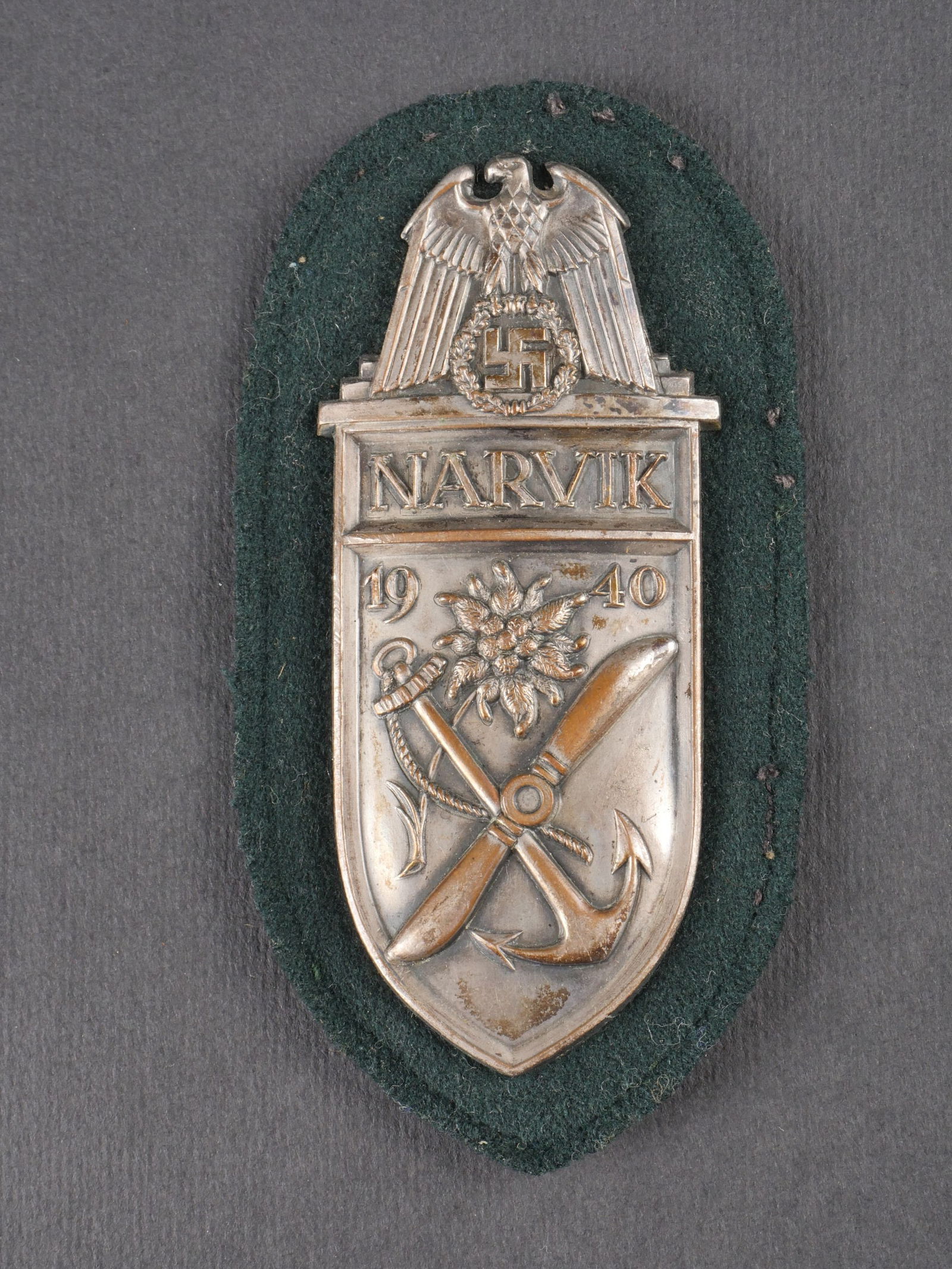 Plaque Narvik. Narvik Shield.: Plaque Narvik en metal embouti nettoye, avec fond en drap vert fonce. Contre-plaque complete. Attaches presentes. a noter une certaine usure et patine de la piece. etat II+. Narvik shield in cleaned s