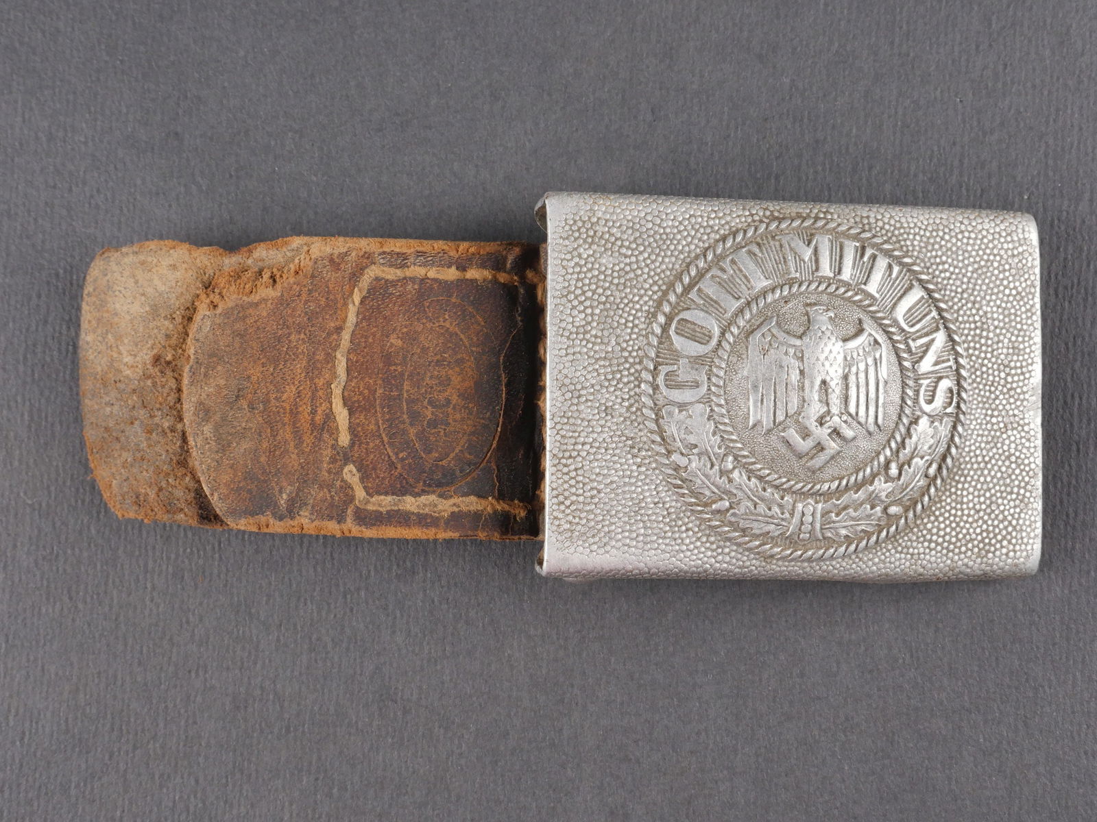 Boucle de ceinturon Heer. Heer belt buckle.: Boucle de ceinturon Heer. Aluminium marque de nombreuses traces d’usure. Fabrication BG. Patte en cuir cousue d’origine. Marquages illisibles. Presente une usure et une oxydation visibles. etat II