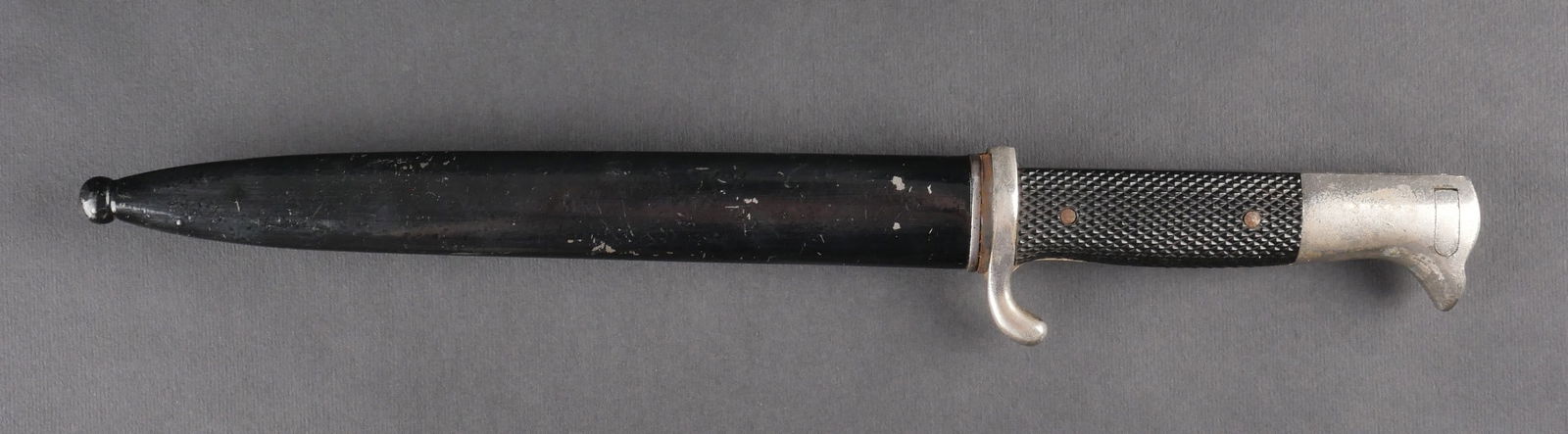 Baionnette de parade.: Baionnette de parade avec garniture en metal nickele, plaquettes en bakelite noire. Fourreau metallique avec peinture noire a 80 %. Quelques bosses et traces d’oxydation. Belle lame marquee du numer