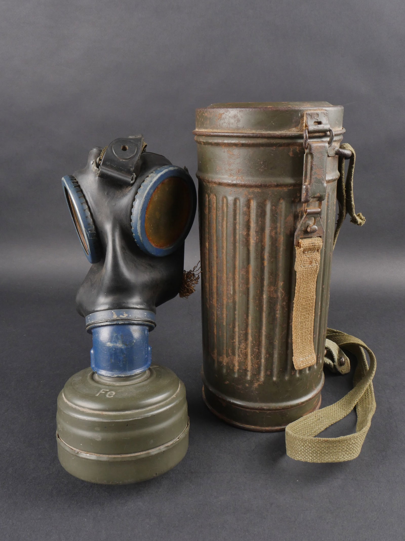 Masque anti-gaz allemand. German Gas Mask.: Masque anti-gaz allemand dans un boitier long en metal, peinture feldgrau conservee a 70 %. Tirette complete, deux autres sangles de remplacement posterieures. Verres de rechange manquants. Masque en 
