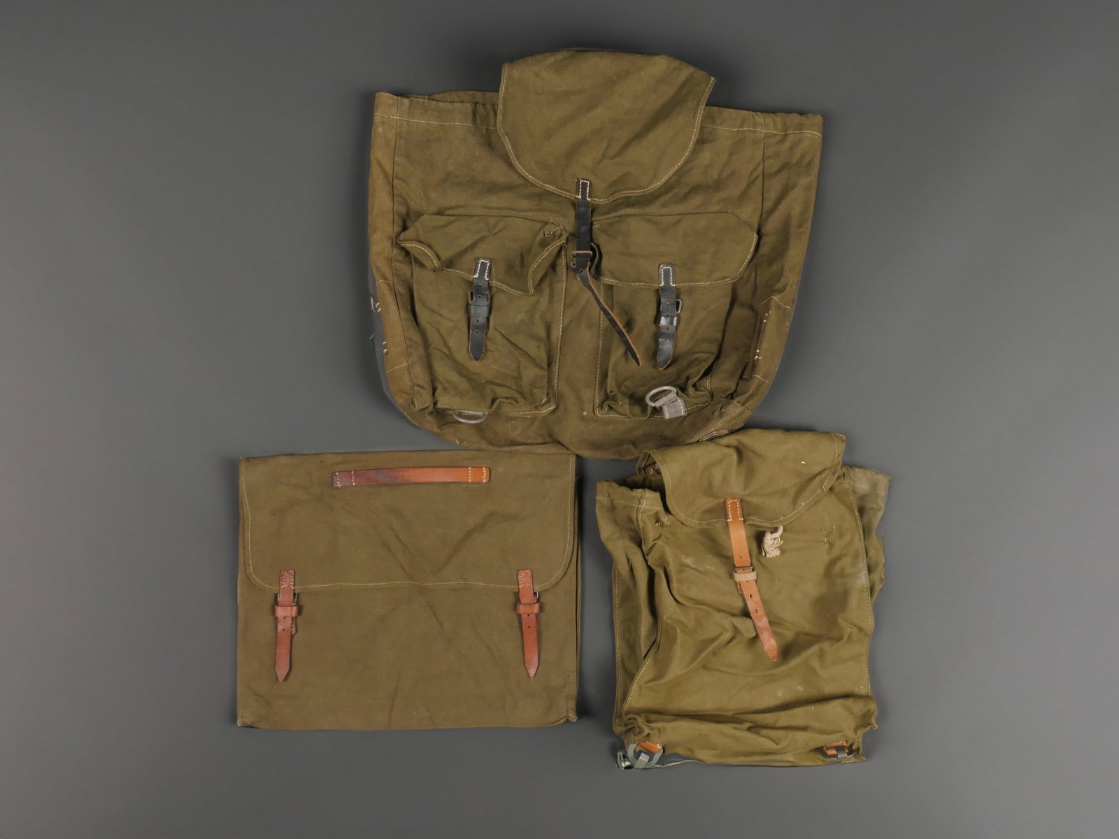 Ensemble de sacs a dos allemand. Set of German backpacks: Ensemble de sacs a dos allemands comprenant un sac a dos en toile feldgrau epaisse et cuir noir, sans cordon de serrage. Deux anneaux sur support en toile gris bleute. Marquages illisibles. Inclus un 