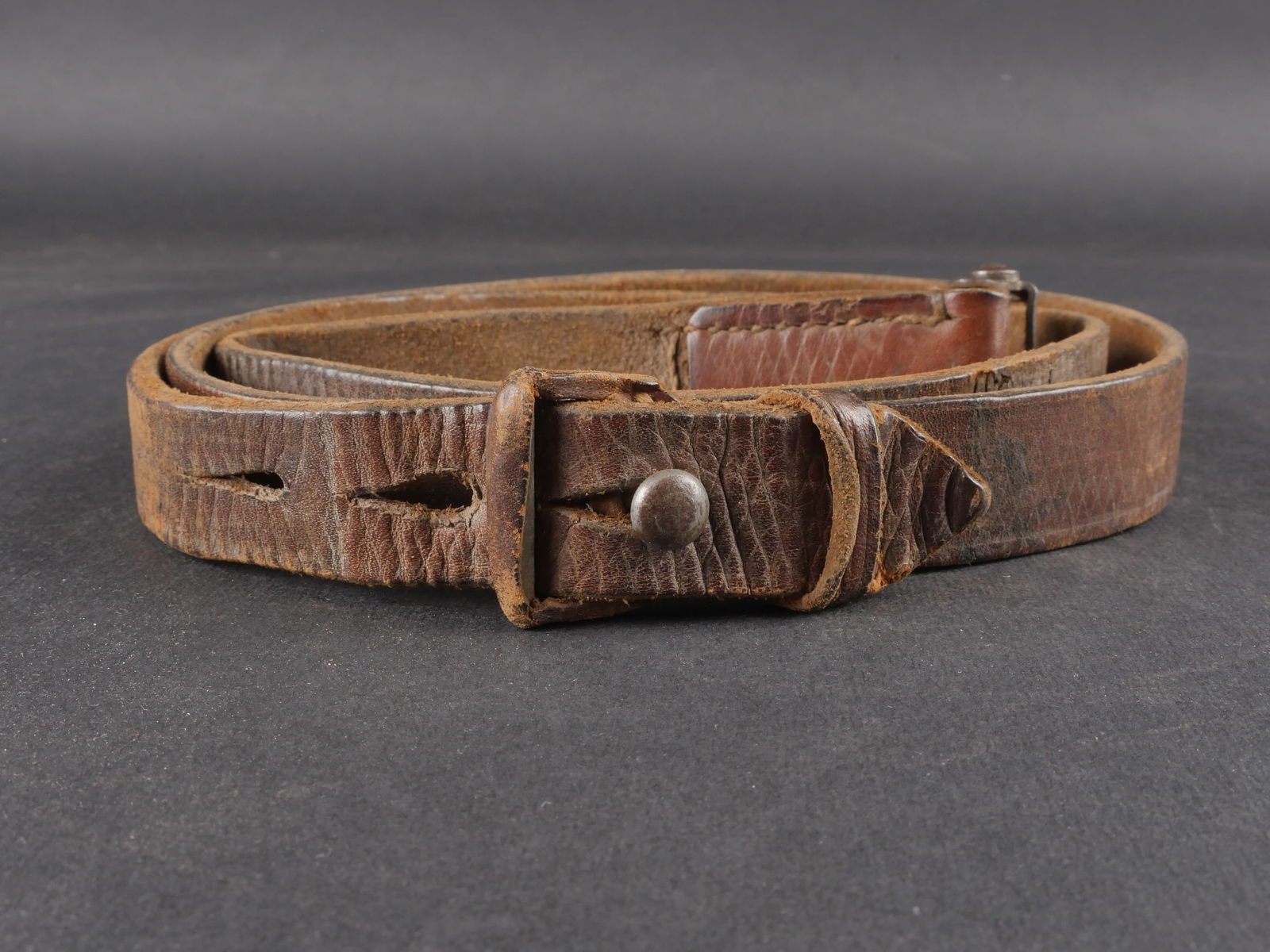 Bretelle de Mauser 98K. Mauser 98K sling: Bretelle de Mauser 98K confectionnee en cuir epais marron a stries, dotee de trois trous de reglage. Boucle et petite patte presentes. Marquages 0/1200/0169 partiellement visibles. Presente une certai