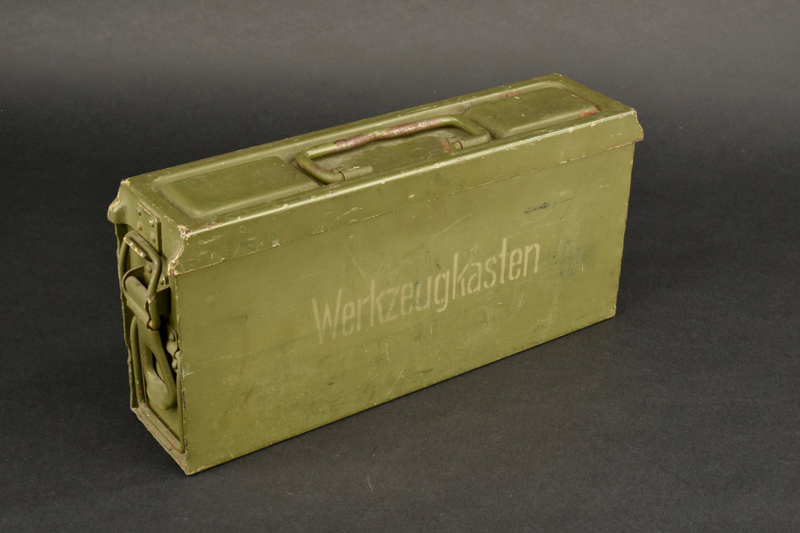 Caisse Werkzeugkasten. Werkzeugkasten crate: Caisse Werkzeugkasten, modele MG en metal, revetue d’une peinture Feldgrau conservee a 80 %. Marquages lateraux au pochoir et marquage «?Werkzeugkasten?» en blanc. Fermetures fonctionnelles. Poign
