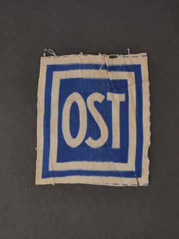 Insigne de travailleur force. Forced laborer badge.: Insigne de travailleur force de l Est. Modele imprime, jamais monte. Les bordures sont partiellement effilochees, un cote presente une dechirure. Trace de colle au dos. A noter une certaine usure et p