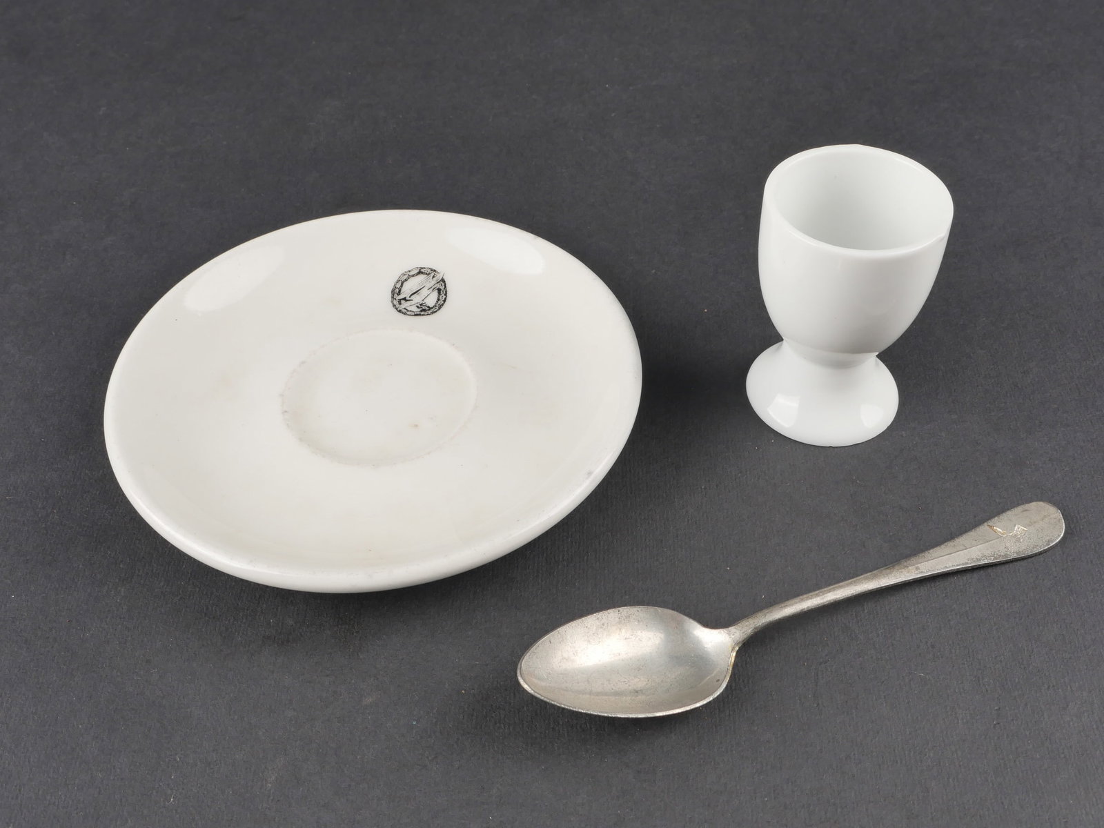 Vaisselle allemande. German Tableware.: Ensemble de vaisselle allemande comprenant un coquetier en ceramique blanche orne d’un bel aigle de la Kriegsmarine, date 1940, une petite coupelle en ceramique blanche portant l’insigne des parac