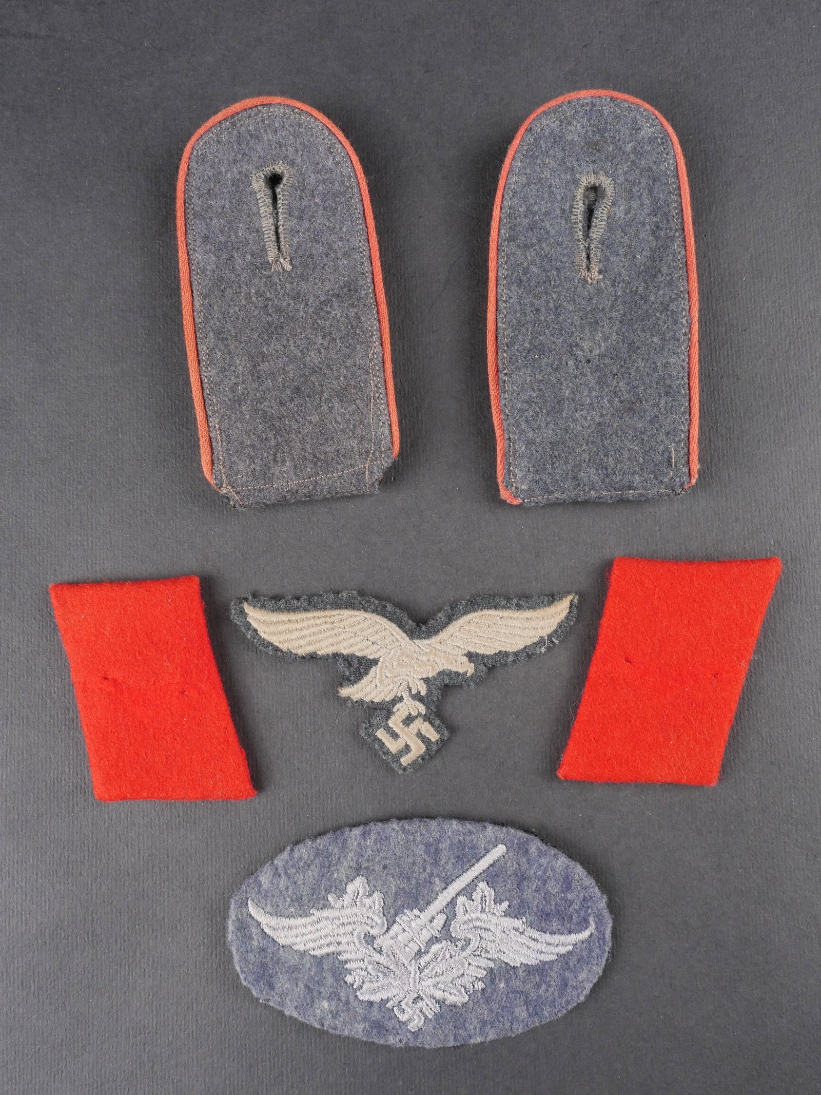 Insignes de la Flak. German antiaircraft insignia.: Insignes de la Flak. Comprend une paire de pattes d’epaule en drap gris-bleu, troupe, lisere rouge passe par le soleil. Insigne de specialite Flak brode sur drap gris-bleu, dos double coton noir. Pa