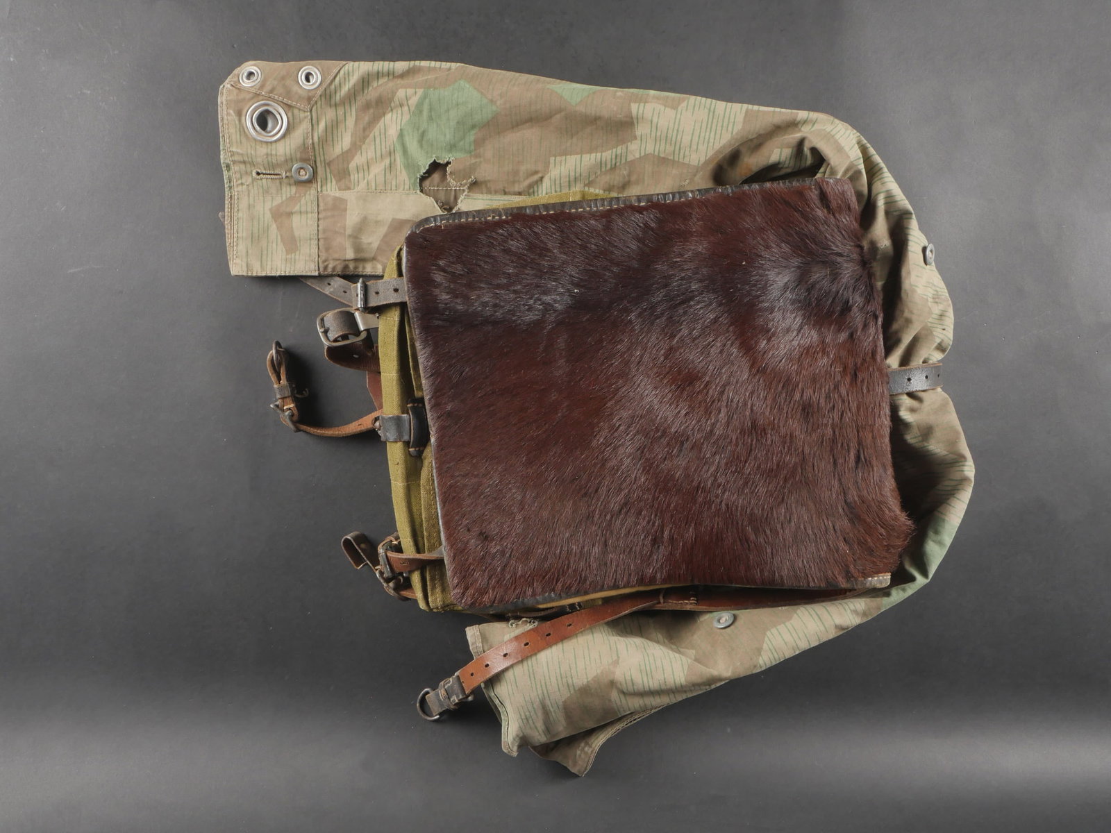 Sac a dos poils de vache. Cowhair backpack: Sac a dos en poils de vache confectionne en epais tissu feldgrau avec toutes les sangles presentes. Poils de vache de couleur marron. Fabrication Berlin 1942. Accompagne d’une toile de tente camoufl