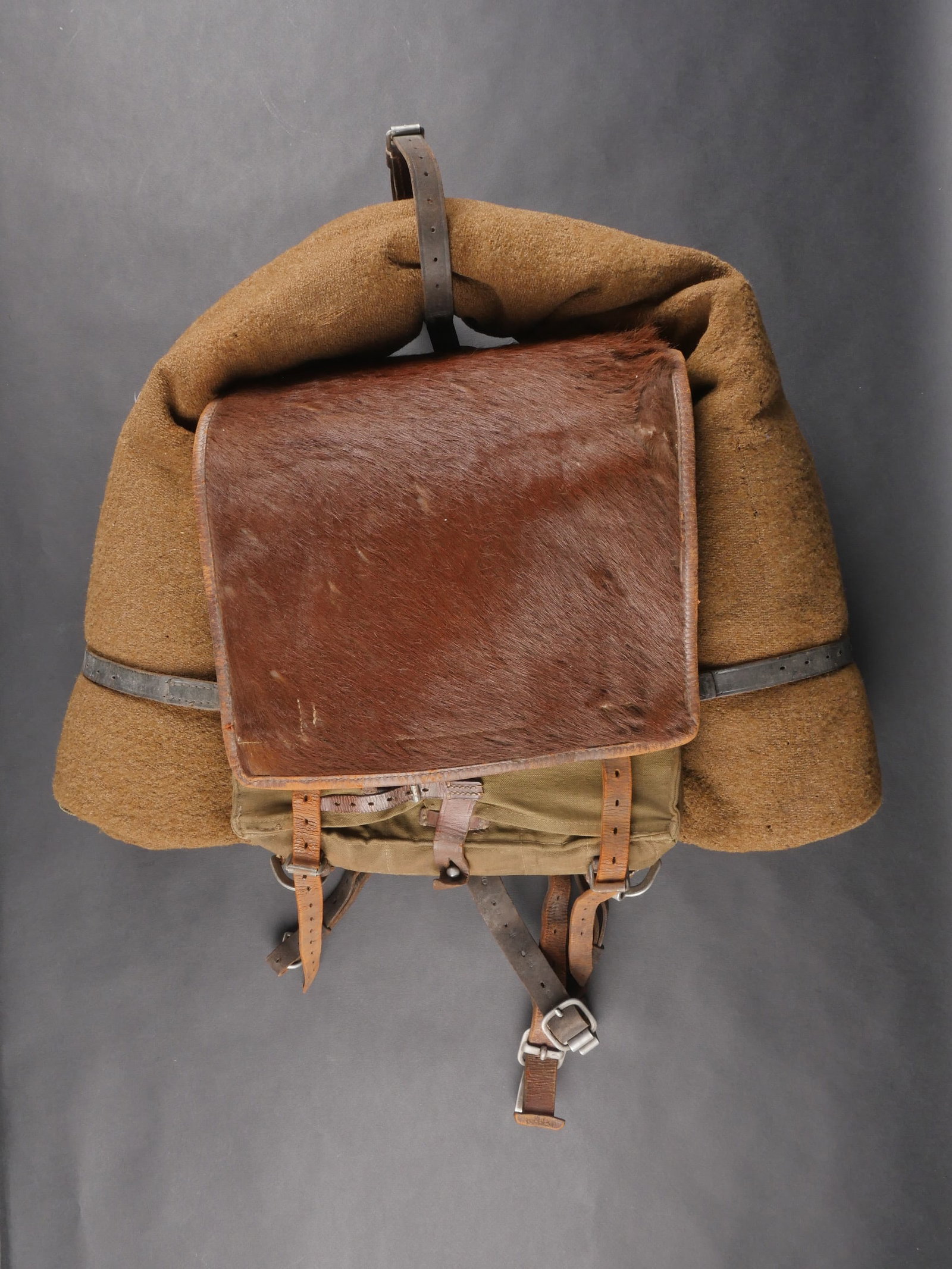 Sac a dos poils de vache. Cowhair backpack: Sac a dos en poils de vache avec structure en forte toile feldgrau. La majorite des sangles est presente. Poils de vache marron. Bretelles completes. Fabrication illisible. Couverture en drap marron r
