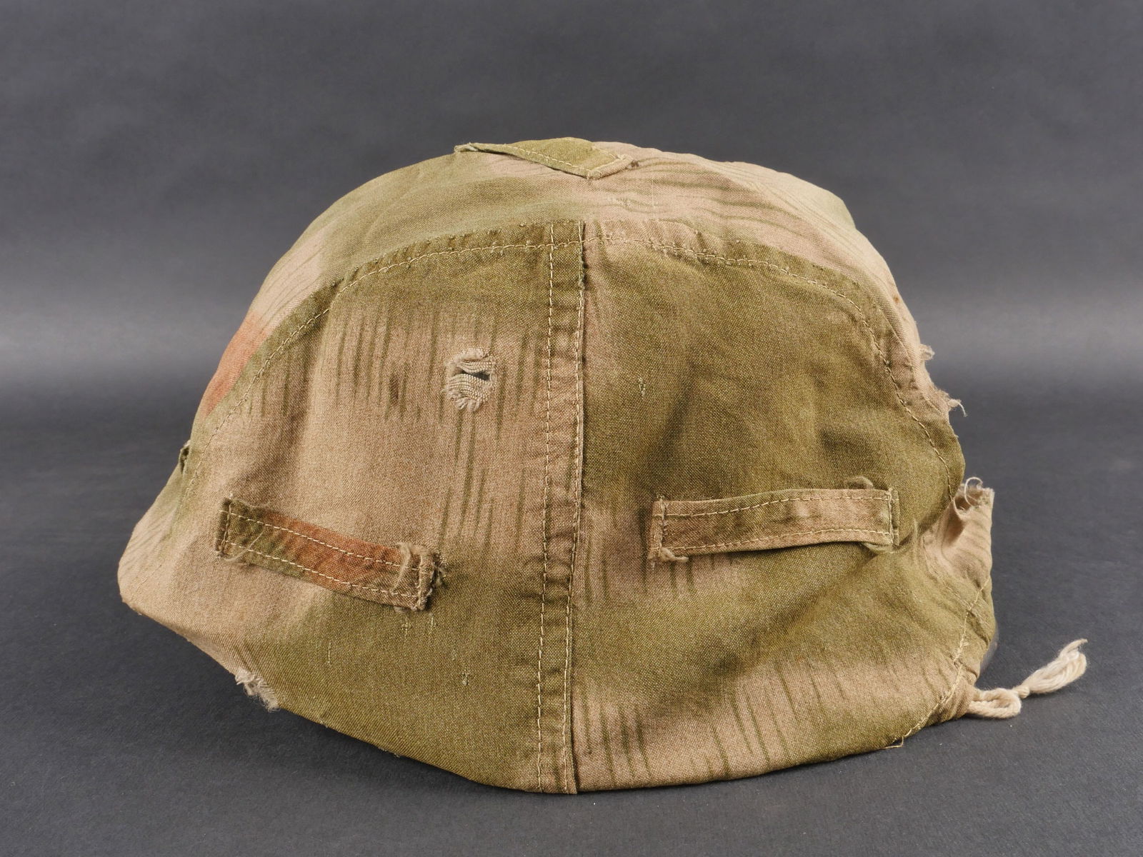 Couvre casque allemand. German cover helmet.: Couvre-casque allemand fabrique en plusieurs parties en tissu camoufle flou. Cordon de serrage posterieur present. Nombreux accrocs et manques. a noter une certaine usure et patine de la piece. etat I