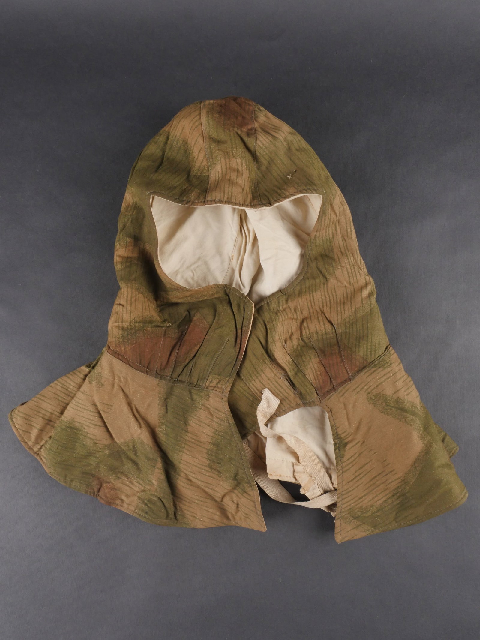 Cagoule camouflee Heer. Heer camouflage hood: Cagoule camouflee de la Heer en tissu camoufle flou, modele reversible blanc. Les oreilles sont protegees par une piece en drap gris. Cordons de serrage presents. Aucun marquage visible. a noter une l