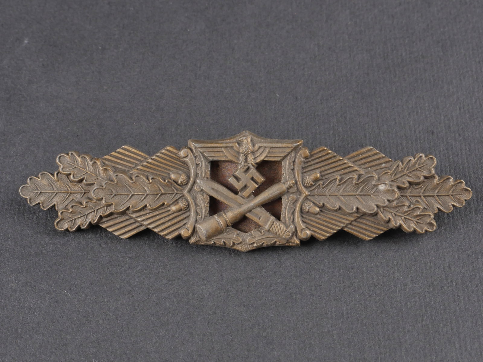 Nahkampfspange. Close Combat Clasp: Nahkampfspange. En metal de teinte bronze a 70 %. Partie centrale oxydee. Attache complete mais tordue. Fabrication Fec WE Peekhaus Berlin AUSF AG MUK Gablonz. a noter une certaine usure et patine de 