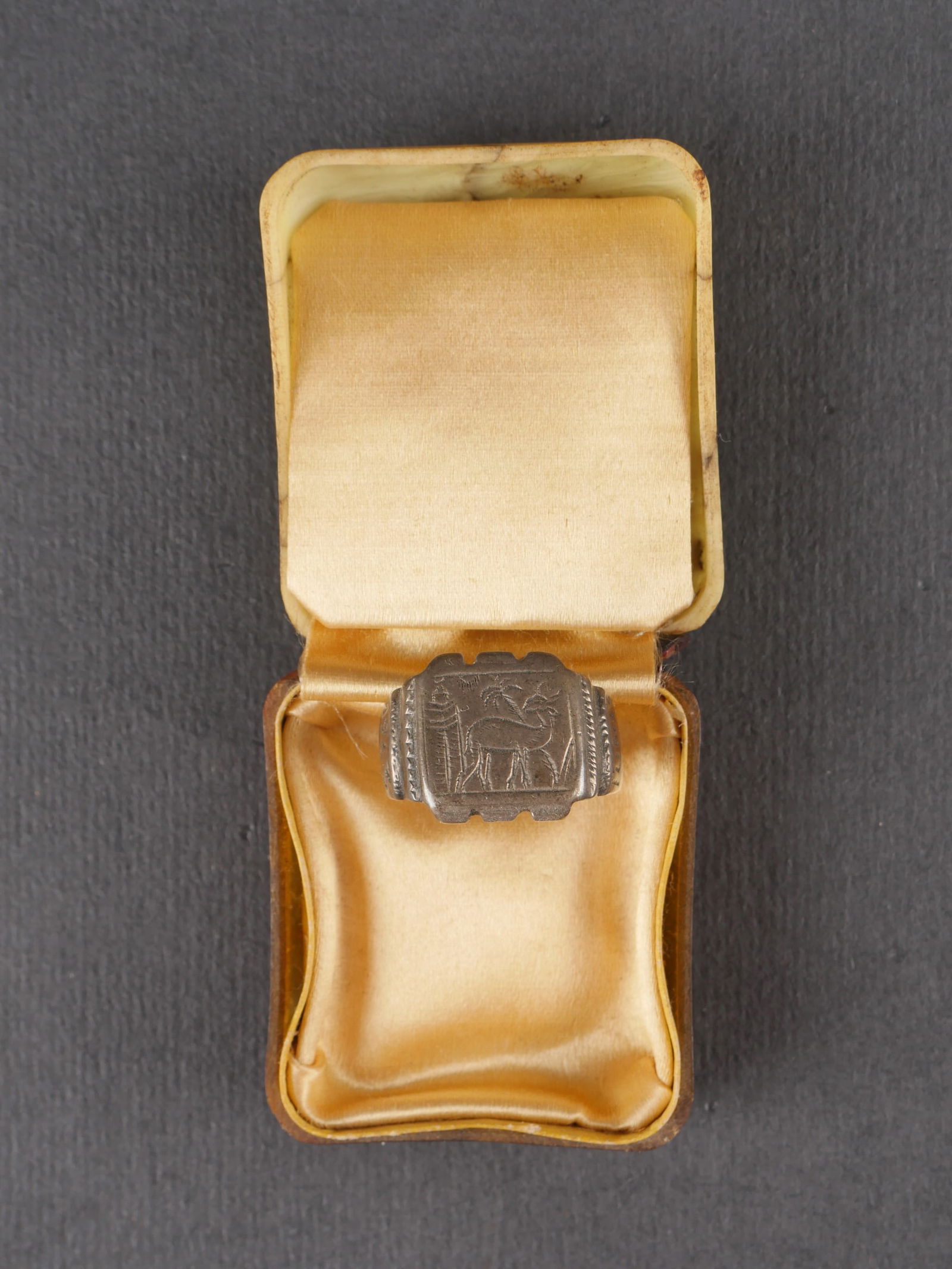 Bague Afrikakorps.: Bague de l’Afrikakorps en metal a decor typiquement africain, marquee Tunis 1943. Presentee dans un ecrin en bakelite dont la charniere est cassee. Ensemble presentant une certaine usure et patine.