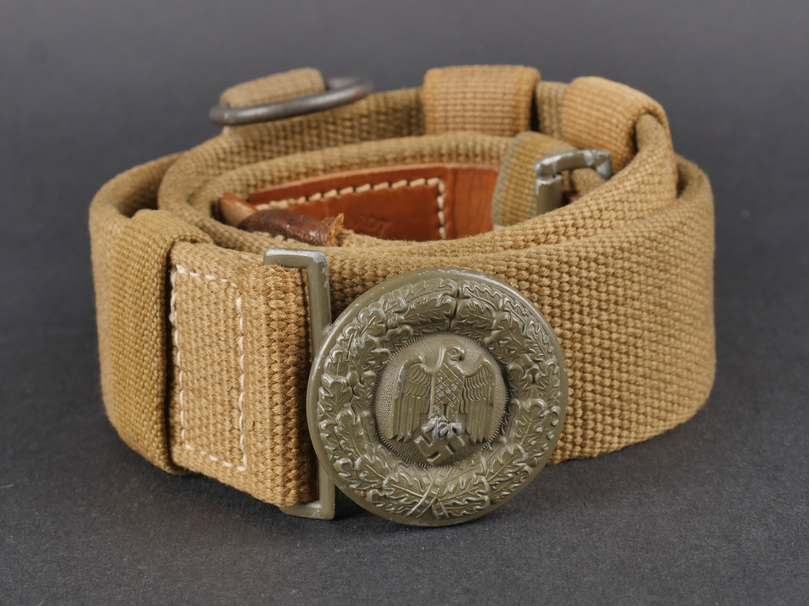 Ceinturon officier AK. Afrikakorps officer belt.: Ceinturon d’officier de l’Afrikakorps en toile jaune sable avec renforts en cuir. Patte de reglage en cuir complete. Marquages G. Reinhardt Berlin 1941. Deux passants en toile presents. Trois rall