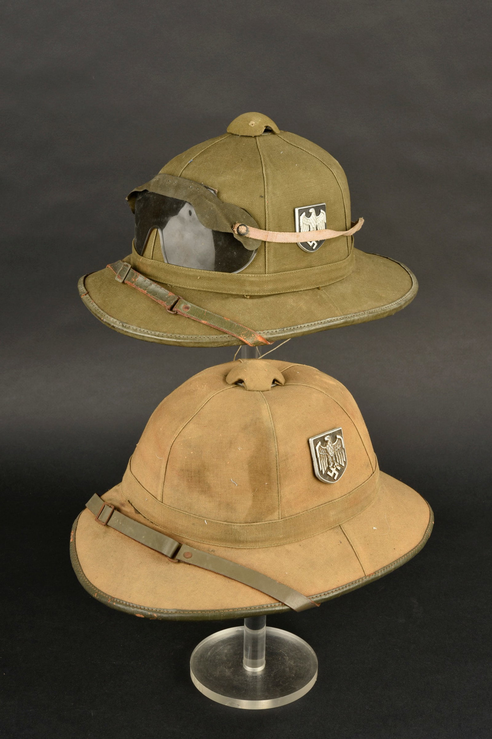 Casques tropicaux de la Heer. Heer tropical helmet: Casques tropicaux de la Heer comprenant un modele en toile beige avec un insigne, pattes cassees. Authenticite non garantie. Structure en liege avec bosses. Jugulaire complete. Interieur double en cot