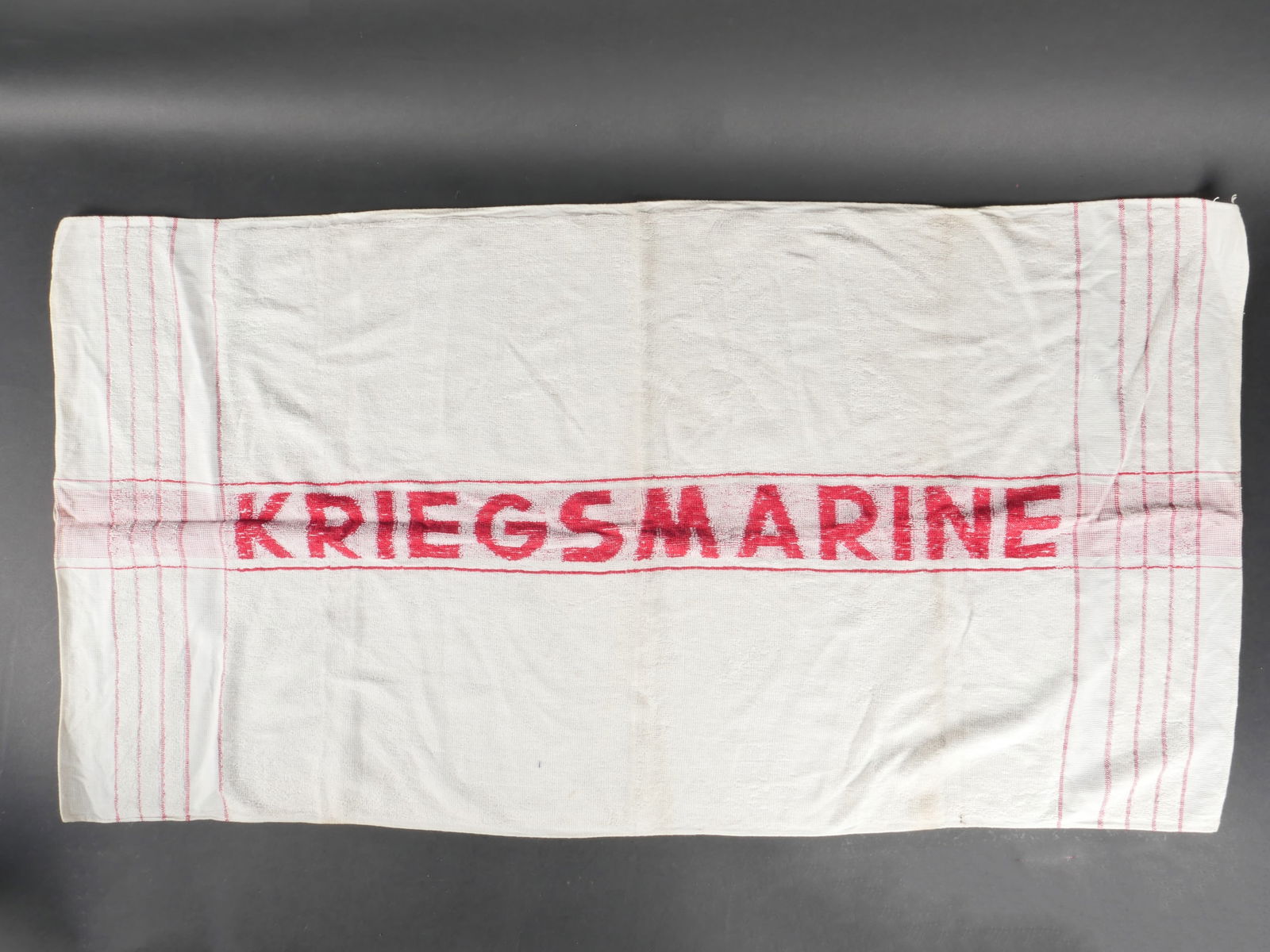 Serviette Kriegsmarine. Kriegsmarine towel.: Serviette de la Kriegsmarine en tissu eponge blanc, ornee de nombreuses bandes rouges. Marquages « Kriegsmarine » rouges. Usure moderee, patine d’usage et quelques taches. etat II+. Kriegsmarine t
