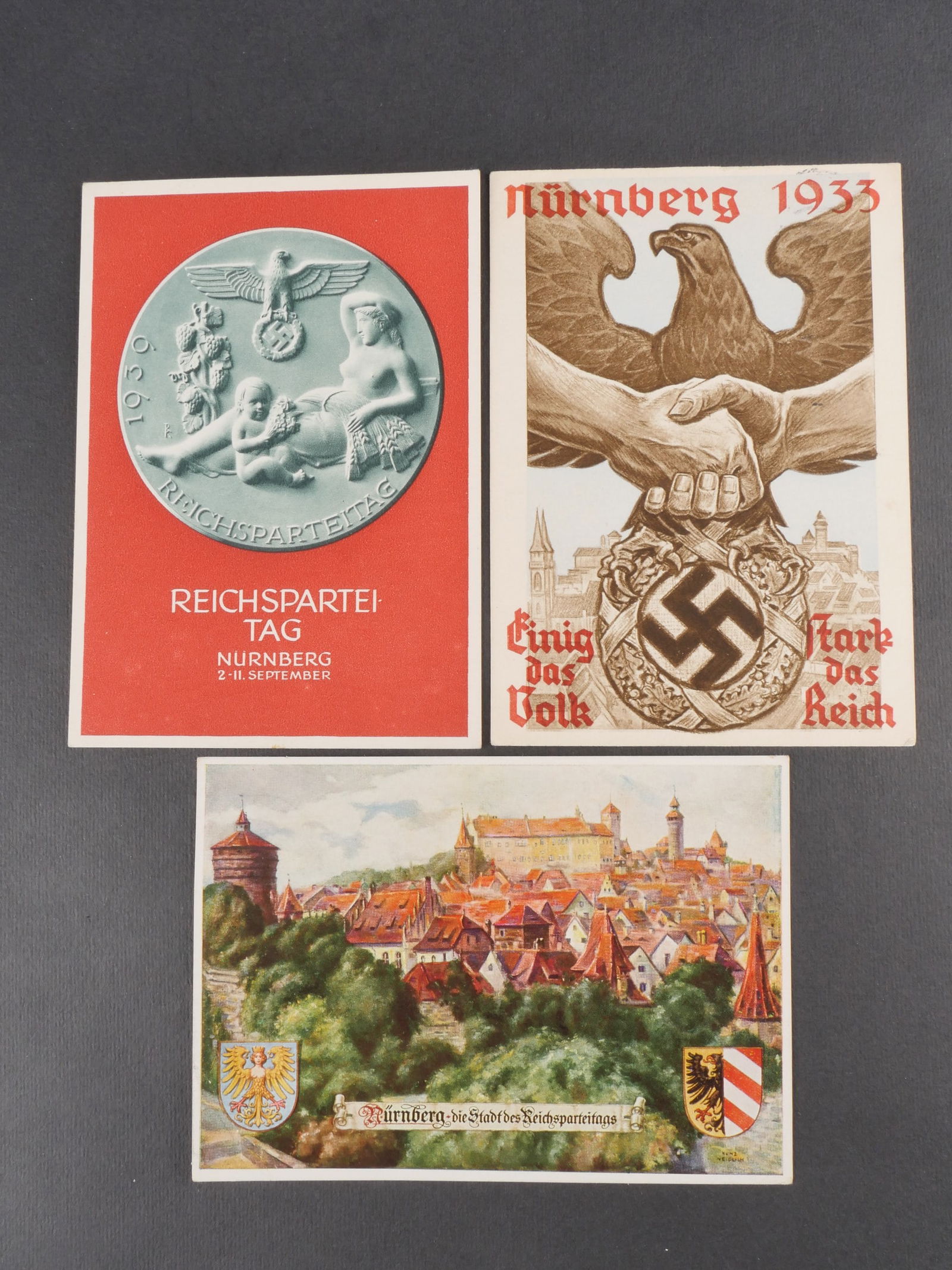 Cartes postales Reichsparteitag. Reichsparteitag Postal cards.: Trois cartes postales du Reichsparteitag, modeles differents, deux avec textes manuscrits au verso. Modeles en couleur. Legere usure et patine. etat I?. Three different Reichsparteitag postcards, two
