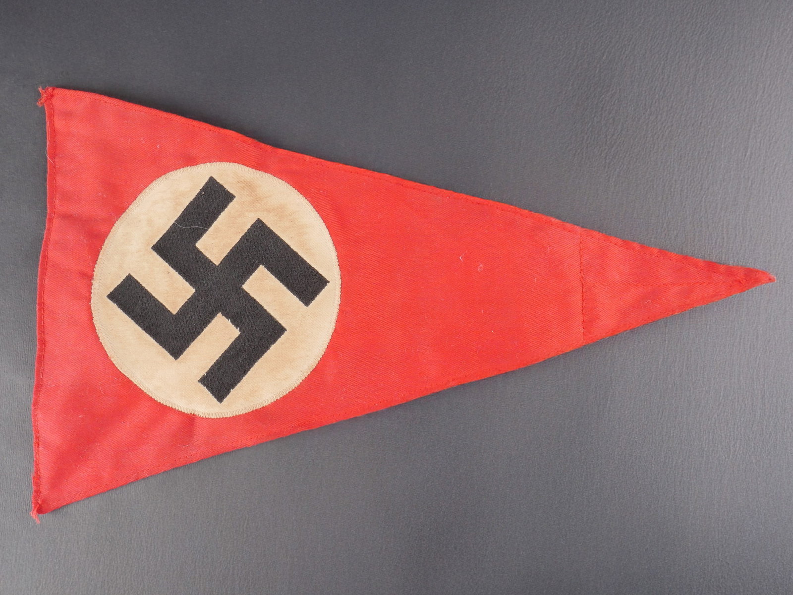 Fanion allemand. German pennant: Fanion allemand. Modele triangulaire en coton rouge epais. Insignes nationaux tisses et cousus. Modele biface. Dimensions 22 x 35,5 cm. Presente une certaine usure, une patine d’epoque et quelques t