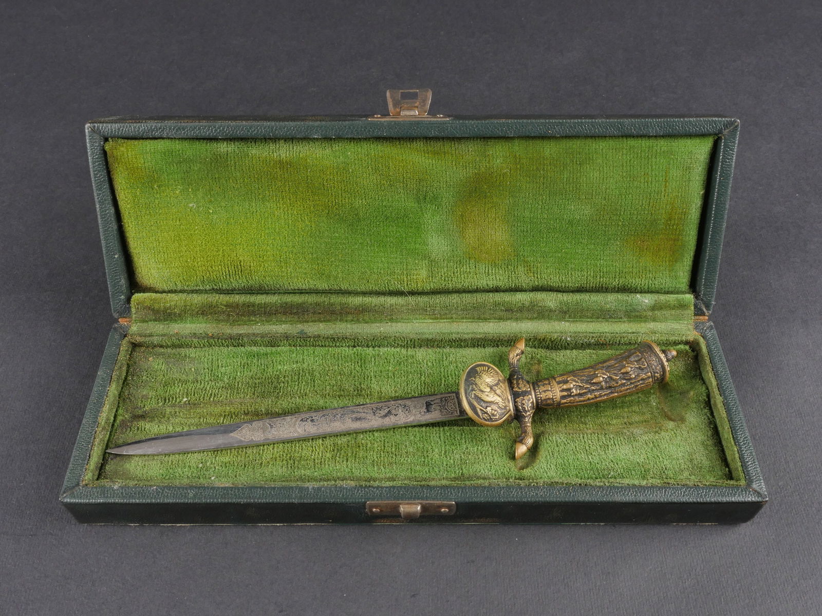 Miniature de dague de chasse. Hunting dagger miniature.: Miniature de dague de chasse presentee en boite. Bel ecrin en cuir vert dont le couvercle est orne de l’insigne de la Federation de chasse allemande ainsi que de motifs floraux. Fermoir complet et f