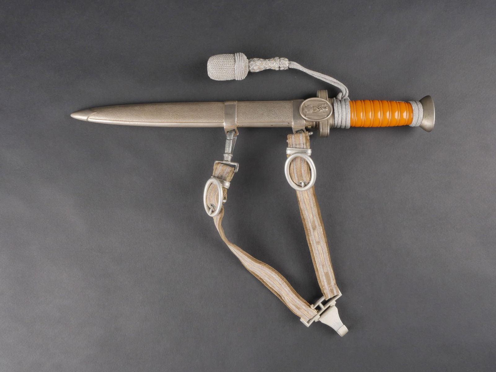 Dague DRK. DRK dagger.: Dague DRK. Garnitures metalliques. Poignee en celluloid orange. Fourreau complet. Belle lame presentant quelques traces d’oxydation. Aucune marque de fabricant visible. Dragonne argentee. Lame leger