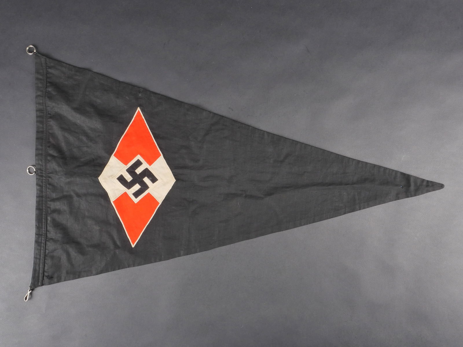 Fanion BDM. BDM pennant: Fanion BDM de forme triangulaire. Recto en tissu noir avec insigne tisse et rapporte, fabrication en plusieurs parties. Revers double de tissu bleu ciel avec insigne runique blanc rapporte. Deux annea