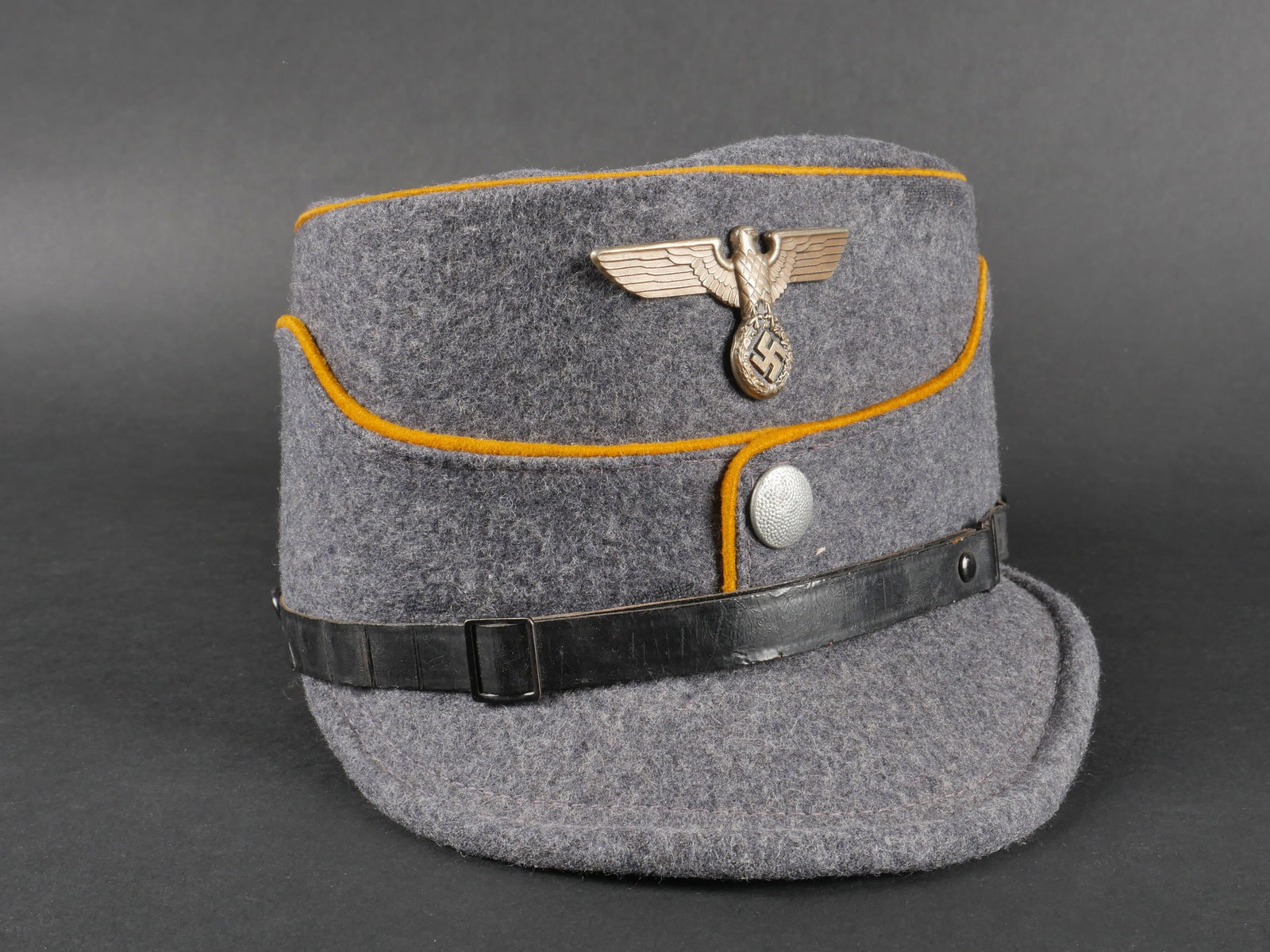 Kepi NSFK. NSFK kepi: Kepi du NSFK confectionne en drap gris-bleu, orne d’un double lisere jaune. Bouton metallique grenele, aigle metallique. Les insignes n’ont pas ete demontes, rendant l’examen des attaches imposs