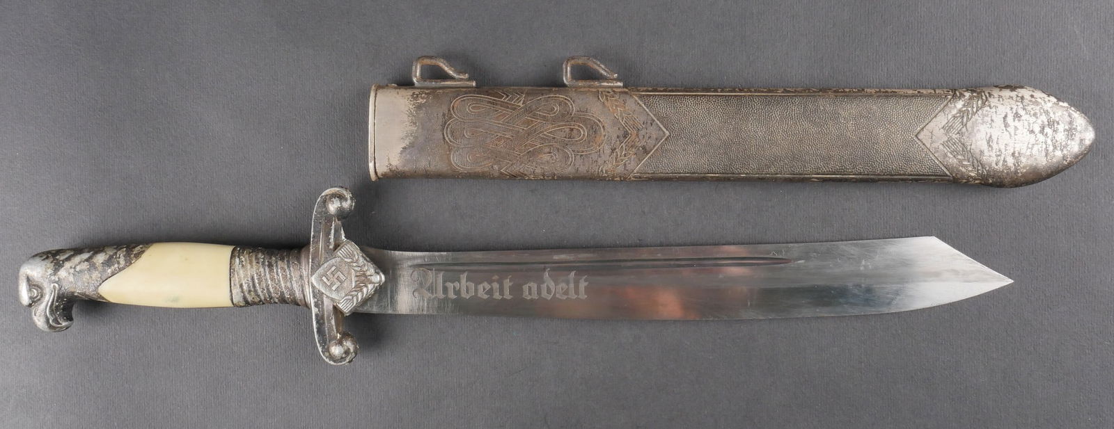 Fendoir d officier du RAD. RZD Officer dagger.: Fendoir d’officier du RAD avec garnitures en metal fortement oxydees. Plaquettes en celluloid blanc. Garde ornee de l’insigne RAD. Fourreau complet, fortement nettoye et oxyde. Lame bien conservee