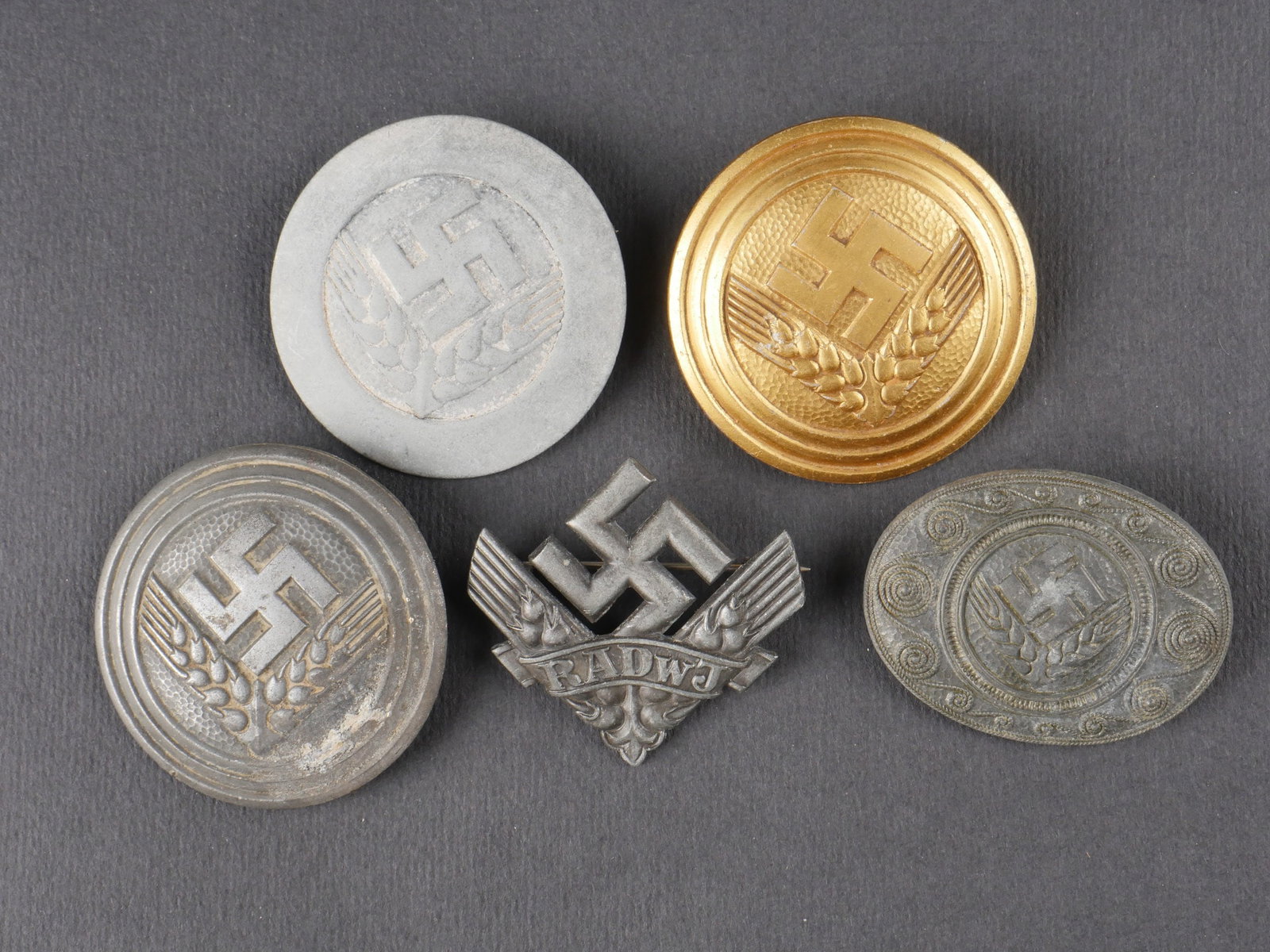 Insignes RAD. RAD insignia.: Ensemble d’insignes RAD comprenant un insigne dore, attache complete, fabrication Assmann 1939, un insigne argente fortement oxyde, attache complete, marquages illisibles, un insigne RADWJ argente a