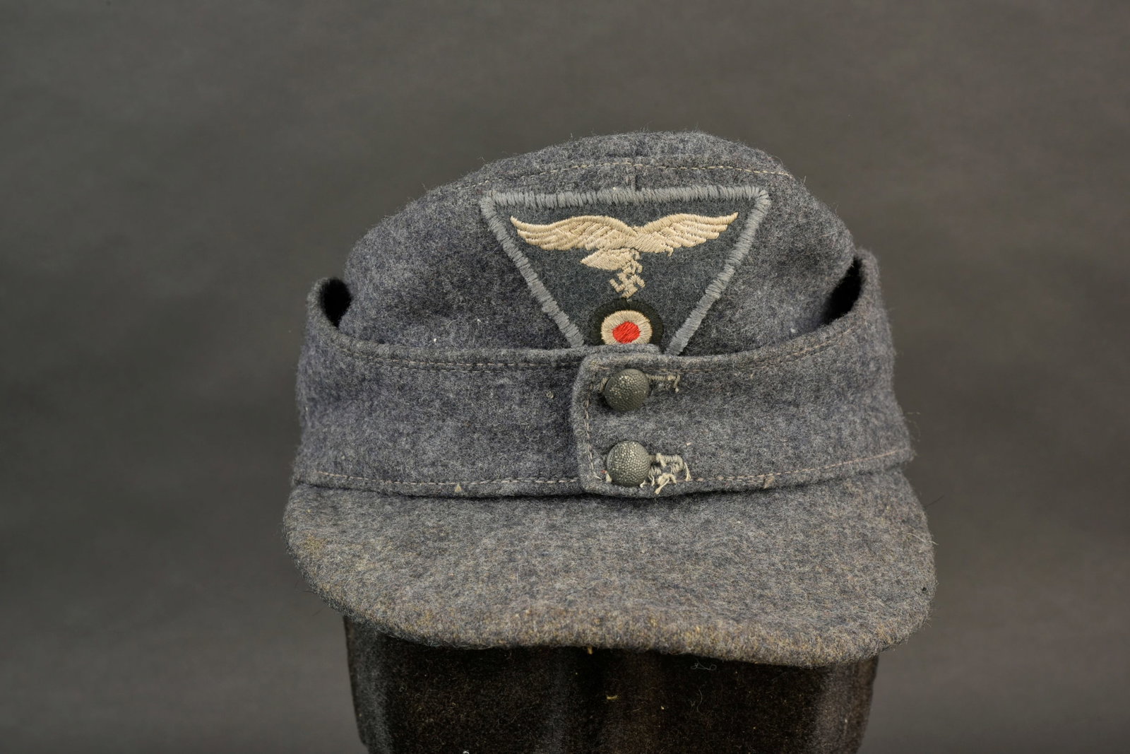 Casquette M-43 de la Luftwaffe. En drap gris/bleu. Deux boutons greneles permettant la fermeture du: Casquette M-43 de la Luftwaffe. En drap gris/bleu. Deux boutons greneles permettant la fermeture du rabat. En couleur d origine. Visiere partiellement tordue. Interieur double en satinette violette. M