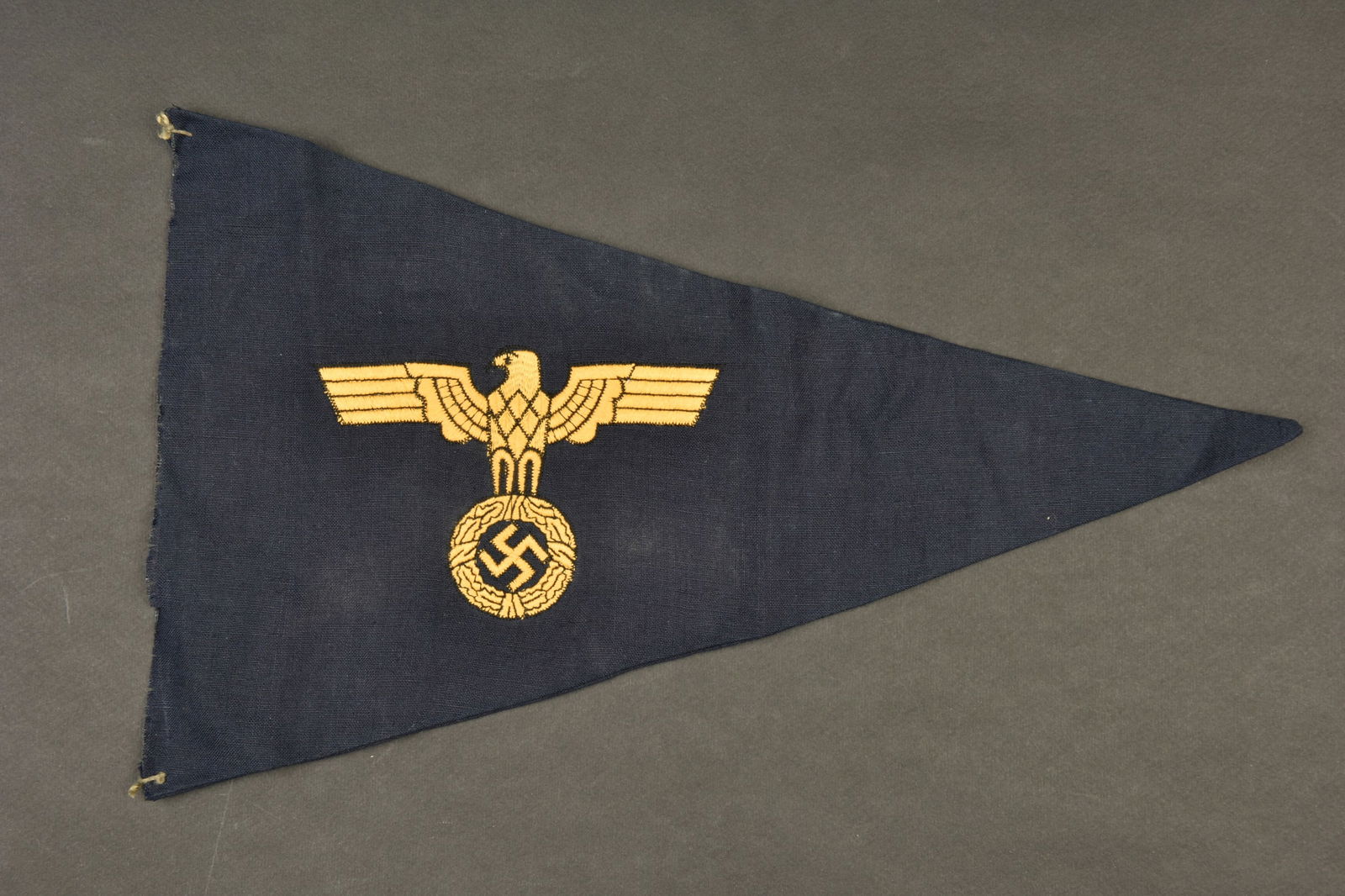 Fanion de voiture de la Kriegsmarine. Triangulaire, en tissu coton bleu marine. Double face. Deux: Fanion de voiture de la Kriegsmarine. Triangulaire, en tissu coton bleu marine. Double face. Deux aigles couleur jaune brodes. La base est completement decousue. Dimensions 23 x 37 cm. L armature meta