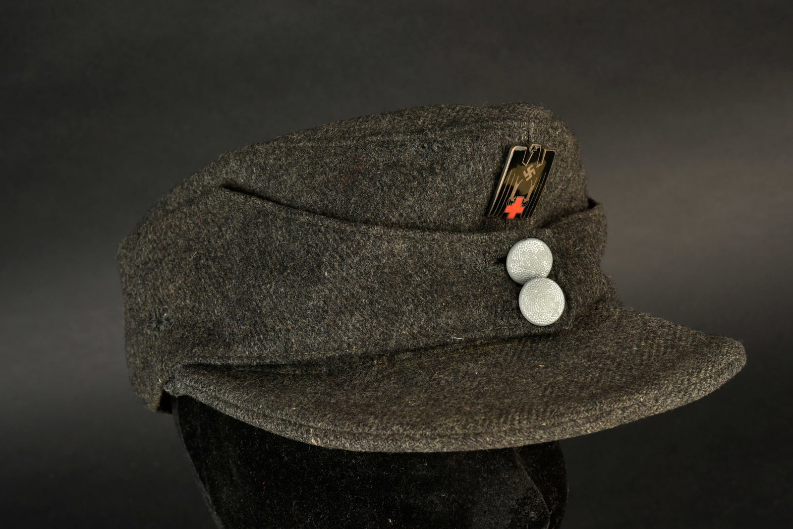 Casquette M-43 de la Luftwaffe. En drap gris fonce. Deux boutons greneles permettant le maintien du: Casquette M-43 de la Luftwaffe. En drap gris fonce. Deux boutons greneles permettant le maintien du rabat. Insigne DRK en metal emaille. L insigne n a pas ete demonte, afin de verifier les attaches. I