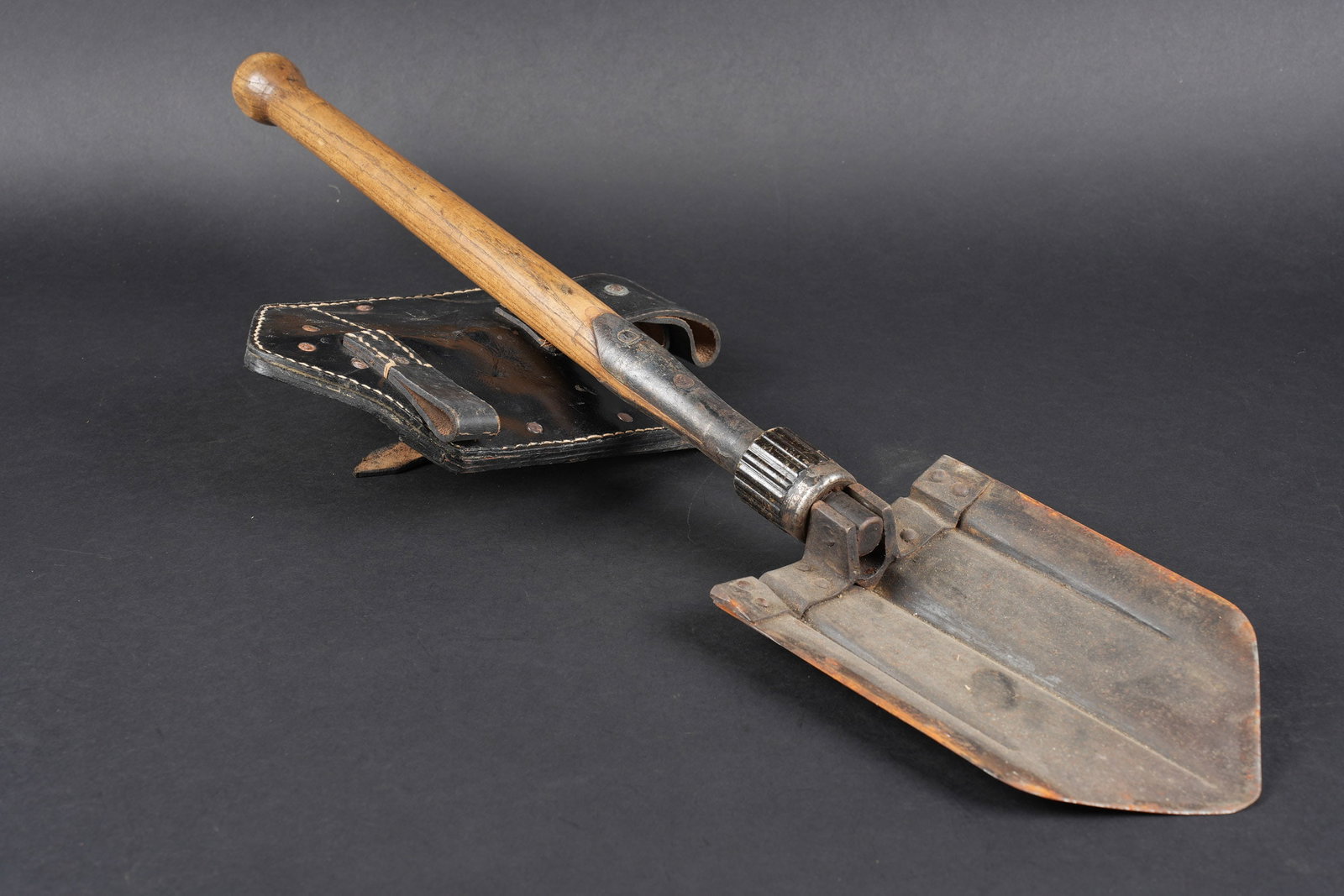 Pelle pliante allemande. German folding shovel.: Pelle pliante allemande. Partie metallique en couleur dorigine a 70%. Sans marquages visibles. Manche en bois complet. Housse pour pelle pliante en epais cuir noir, avec renforts en metal. Toutes les 