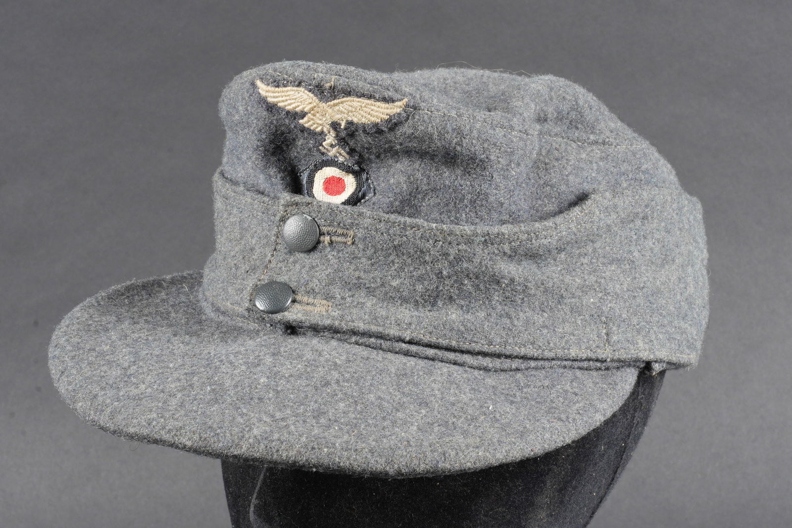 Casquette M43 LW. Luftwaffe M-43 cap.: Casquette M-43 de la Luftwaffe. En drap gris/bleu. Rabat fermant par deux boutons greneles gris/bleu. Aigle brode, cousu machine. Cocarde Bevo, egalement cousue machine. Visiere en bon etat, quelques