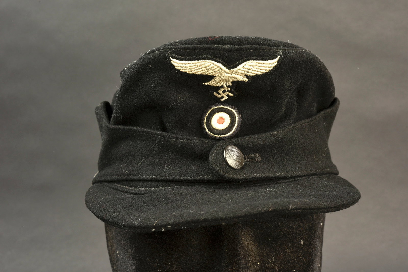 Casquette Hermann Goring. Hermann Goring M-43 cap.: Casquette Hermann Goring. En drap noir. Un bouton lisse fermant le rabat. Aigle de la Luftwaffe et cocarde sur fond noir, cousus main. Visiere presentant quelques craquelures. Demi bandeau de sudation