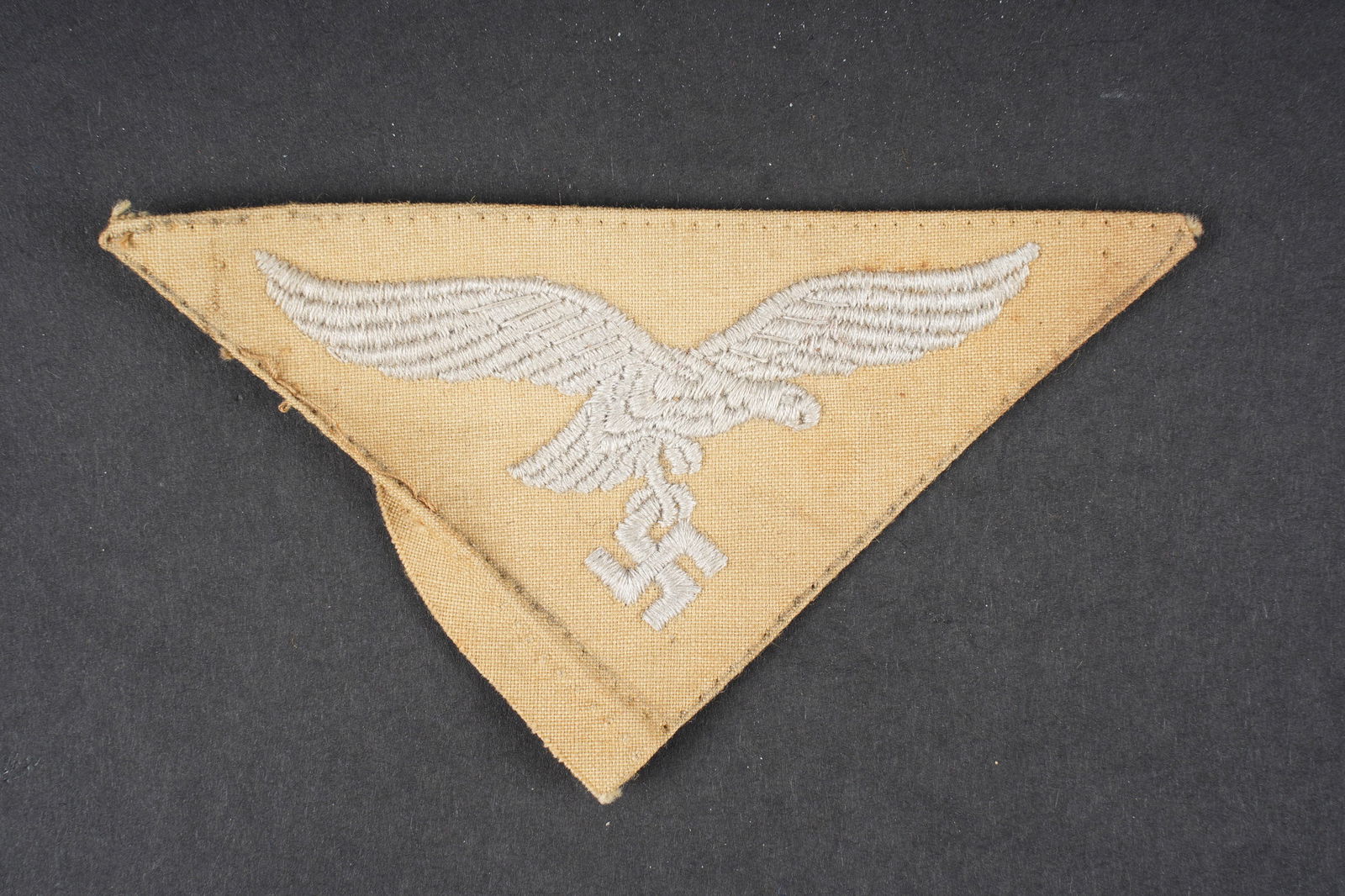Insigne LW. Luftwaffe insignia.: Insigne tropical de la Luftwaffe. Bel aigle de poitrine, triangulaire, brode. Visiblement demonte d une vareuse. A noter une certaine usure et patine de la piece, ainsi que quelques taches. Etat II +.