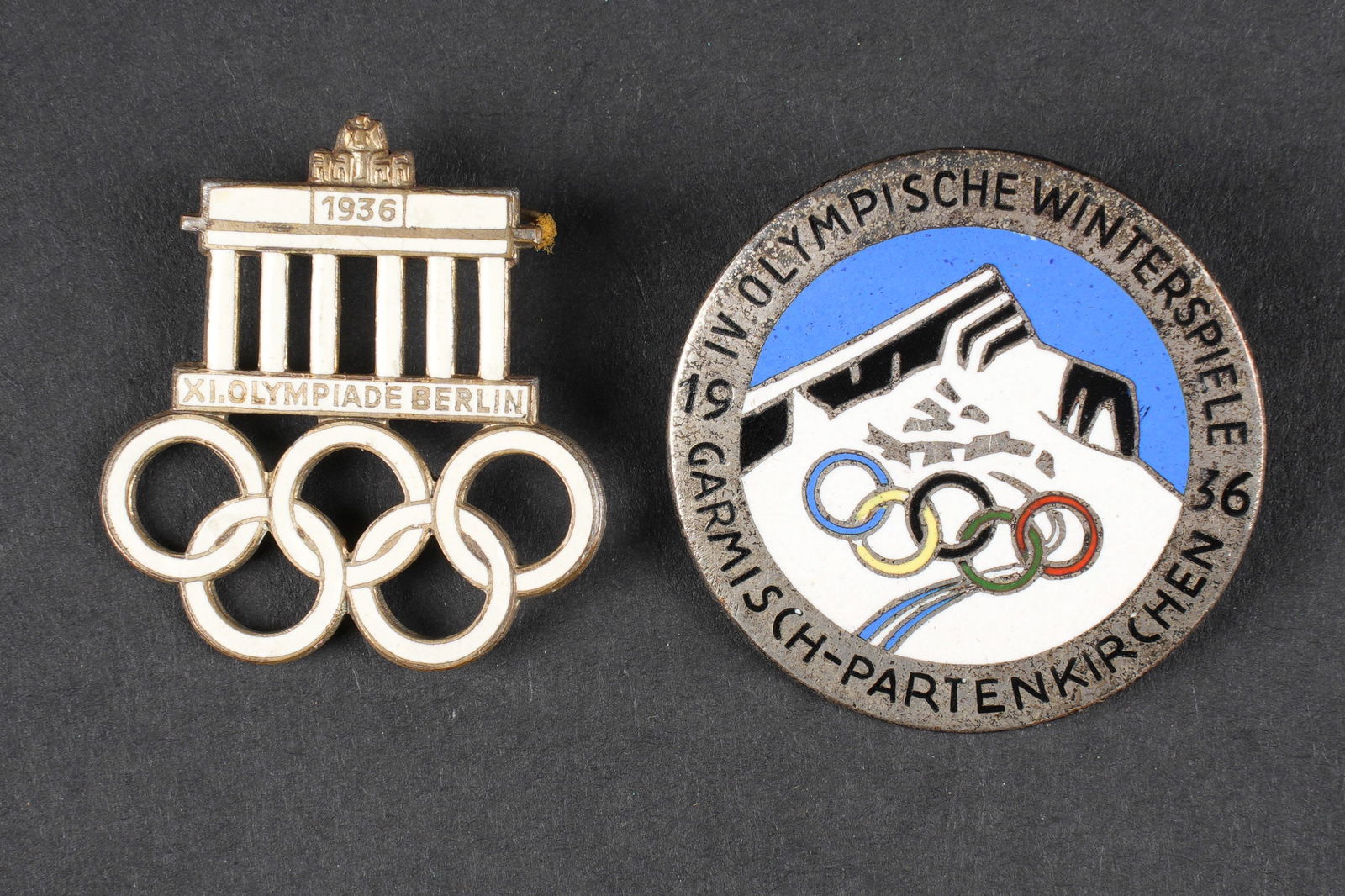 Insignes des jeux olympiques. German olympic games insignia.: Insignes des jeux olympiques. Comprenant un insigne en metal emaille des jeux olympique de Berlin 1936, attache complete, sans marquages visibles. Un insignes des jeux olympique de Garmisch Partenkirc
