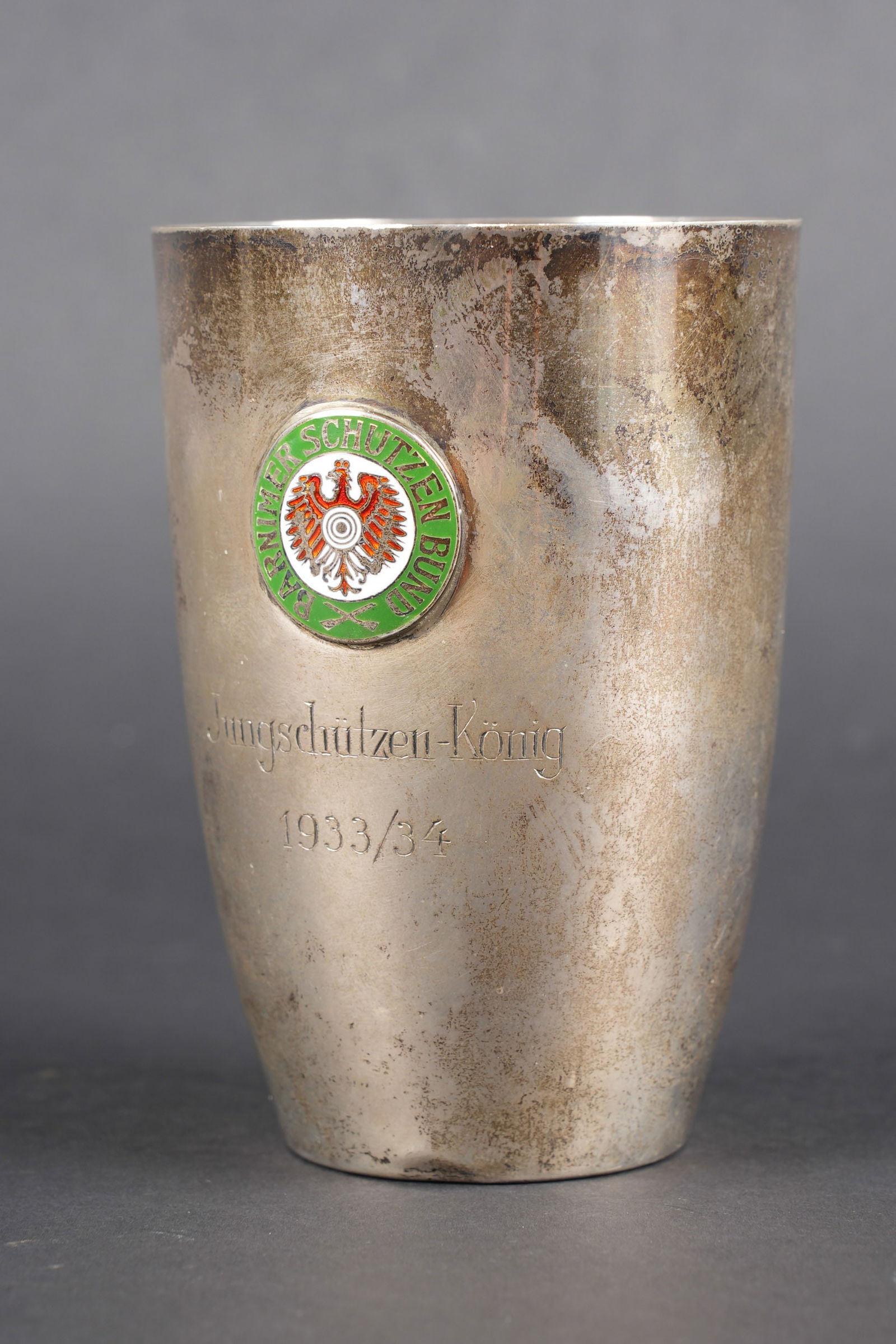 Gobelet prix de tir. German Shooting award goblet: Gobelet prix de tir. En metal, couleur argent. Insigne en metal emaille, marque Barnimer Schutzen Bund. Mention Jungschutzen Konig 1933/1934. Poincon d argenture 800. A noter une certaine usure et pat