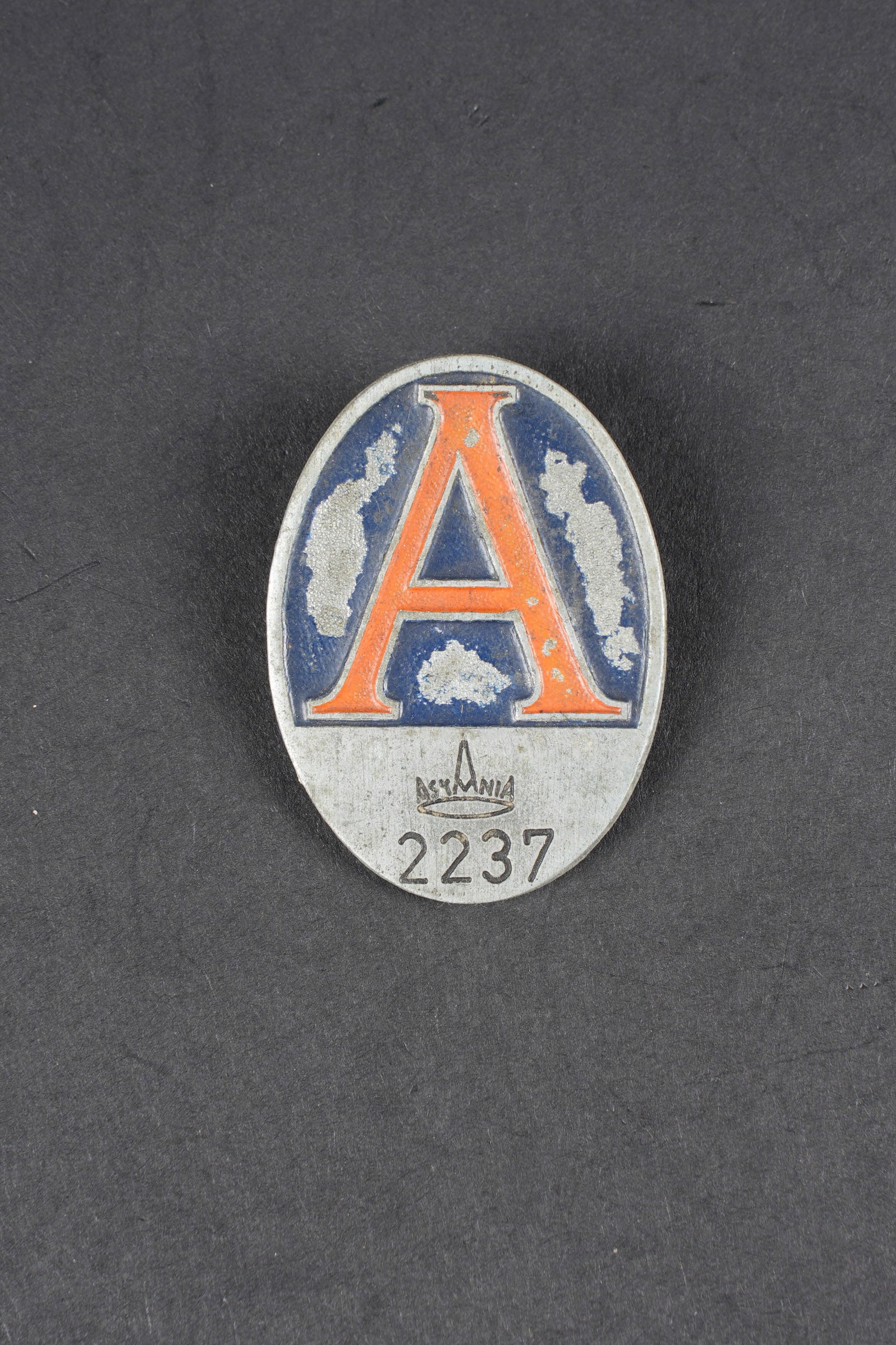 Plaque de travailleur allemand. German worker badge: Insigne de travailleur allemand de l usine Askania. En metal, fabrication en relief. Peinture partiellement absente. Indication de l usine Askania, qui produisait des montres et instruments pour la Lu