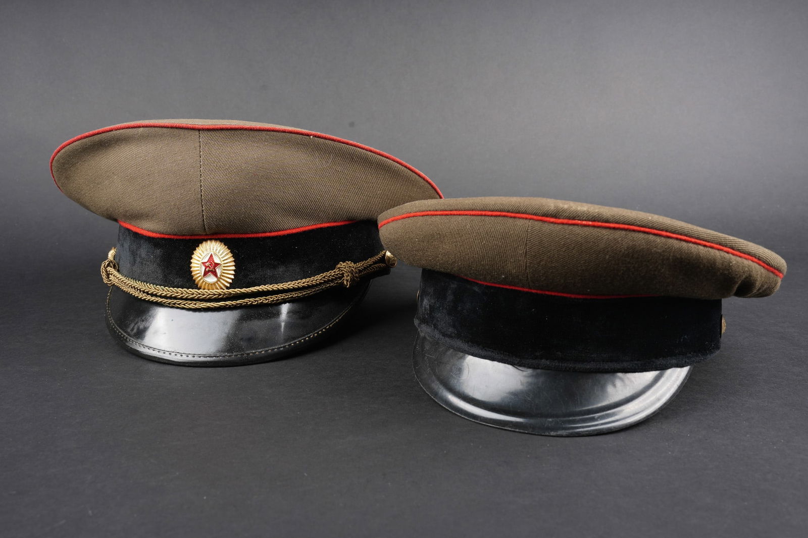 Casquette russe. Russian military service cap: Lot de 2 casquettes russes periode guerre froide. En tissu kaki, passepoils rouges, bandeau velours noir. Boutons a l etoile sovietique, une datee 1958 avec jugulaire, l autre sans. Usure d usage.