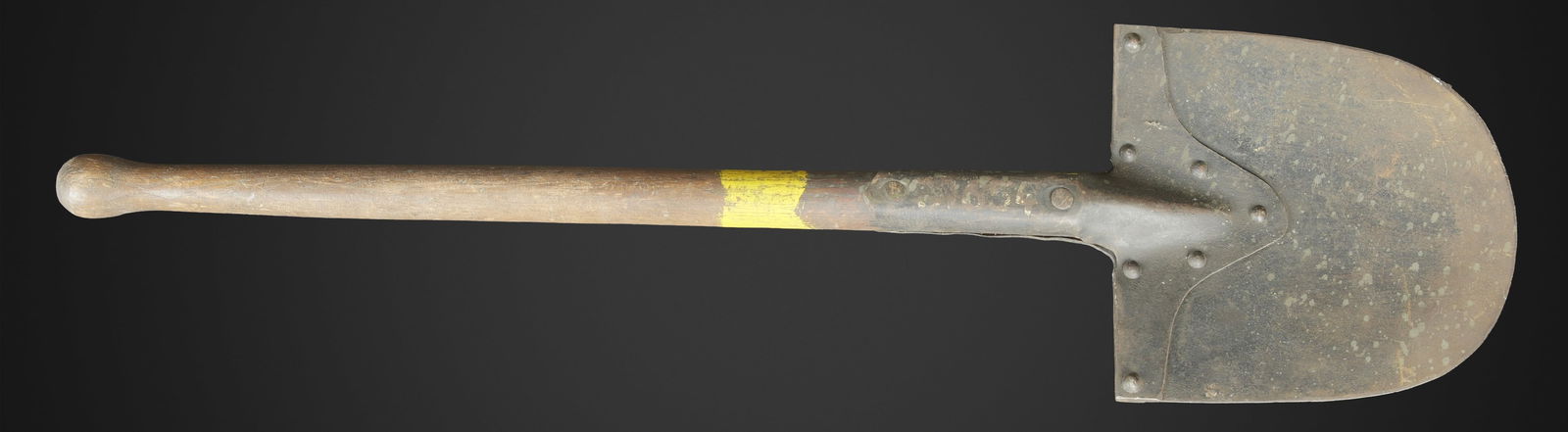 Pelle WH. WH entrenching shovel: Pelle WH. Manche en bois, bout arrondi. Bande jaune faisant le tour du manche. Partie metallique en metal, peinture noire a 70%. Restes de marquages illisibles. Longueur 84 cm. A noter une certaine us