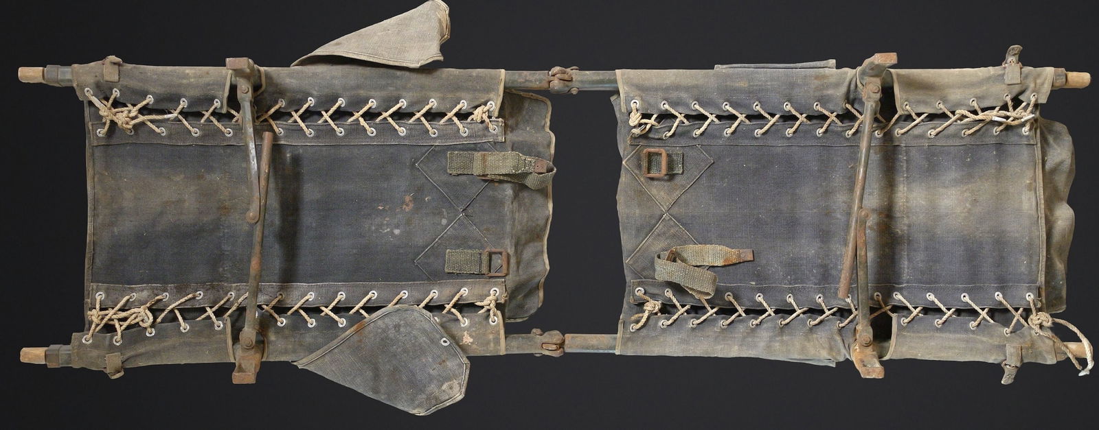 Brancard WH. WH stretcher: Brancard WH. Modele en deux parties. Toile de couleur gris bleu. Nombreux accrocs et taches visibles. Armature en bois et metal. Sans marquages visibles. Les cordelettes sont en partie absentes. A