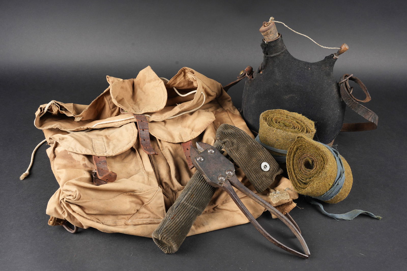 Ensemble d equipements. Set of equipment: Ensemble d equipements. Comprenant un bidon 1877 de deux litres avec sa housse en drap gris de fer bleute. Un sac a dos ersatz en toile cachou, bretelles en toile kaki a crochet, tampon de reception i