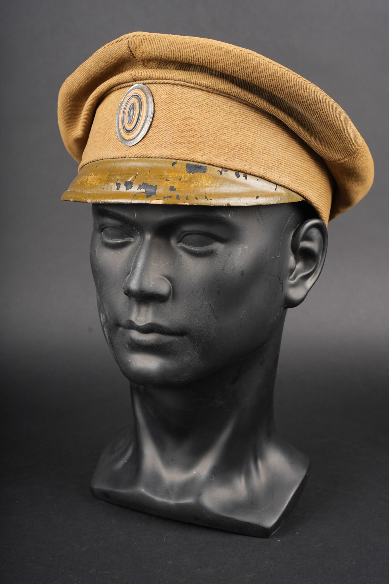 Casquette russe 1909. Russian cap model 1909: Casquette russe 1909. Casquette modele 1909 confectionnee en toile de coton cachou, visiere en fin cuir noir recouverte de kaki. Passepoil de la meme couleur que la casquette, cocarde ovale en metal p