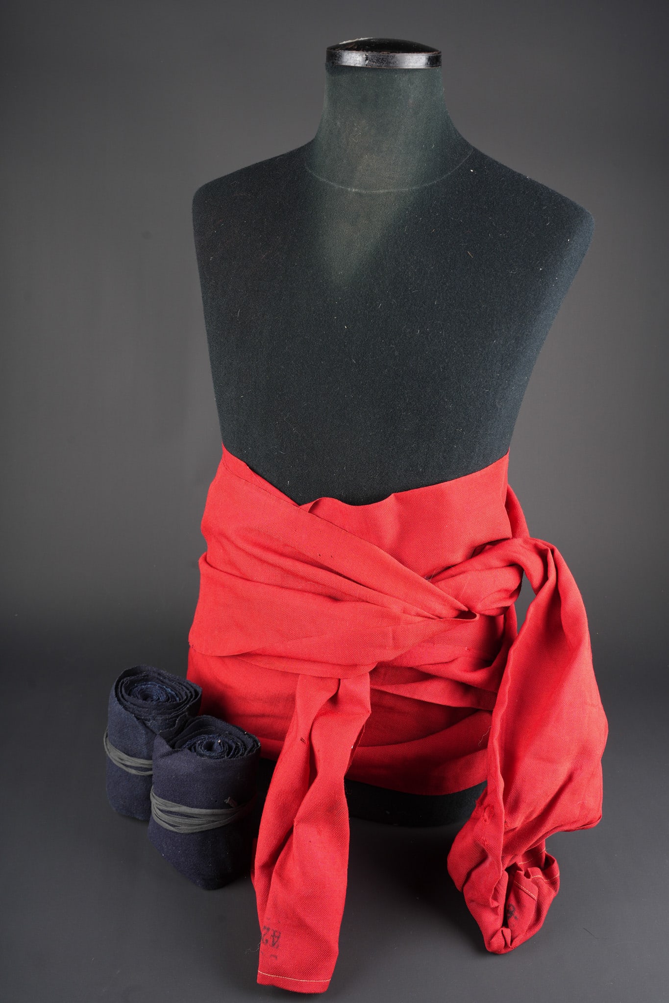 Lot d effets zouaves. Zouave effects grouping.: Lot d effets zouaves. Comprenant une ceinture de tradition garance matriculee, largeur 39cm, longueur 425cm. Une paire de bandes molletieres droites en drap bleu fonce, confectionnees en deux parties,