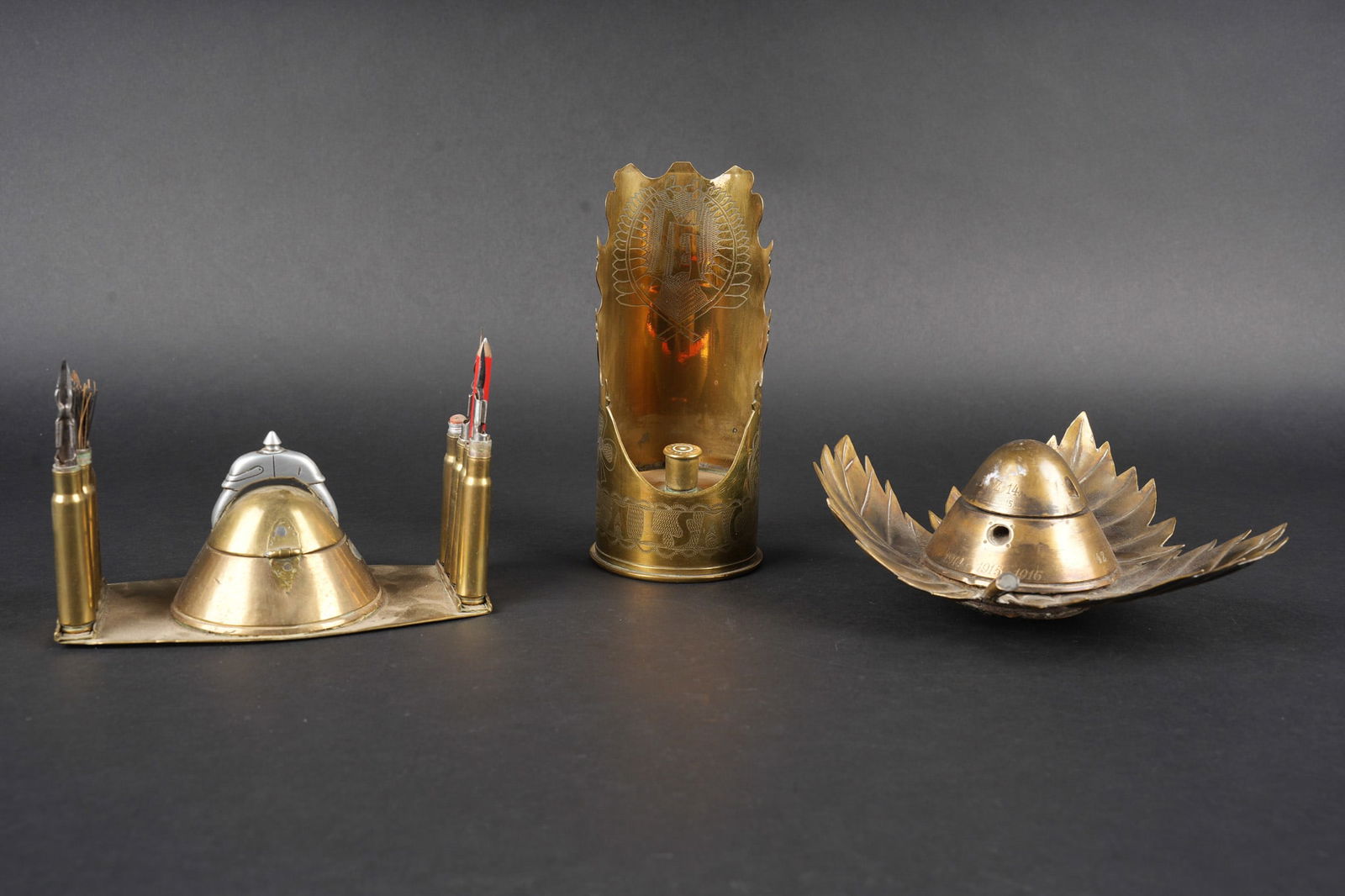 Lot artisanat de tranchees. Lot of trench art: Lot artisanat de tranchees. Comprenant un encrier realise a partir d une ogive avec un casque a pointe de profil en aluminium, de chaque cote on trouve des lames chargeurs de Mauser et les douilles