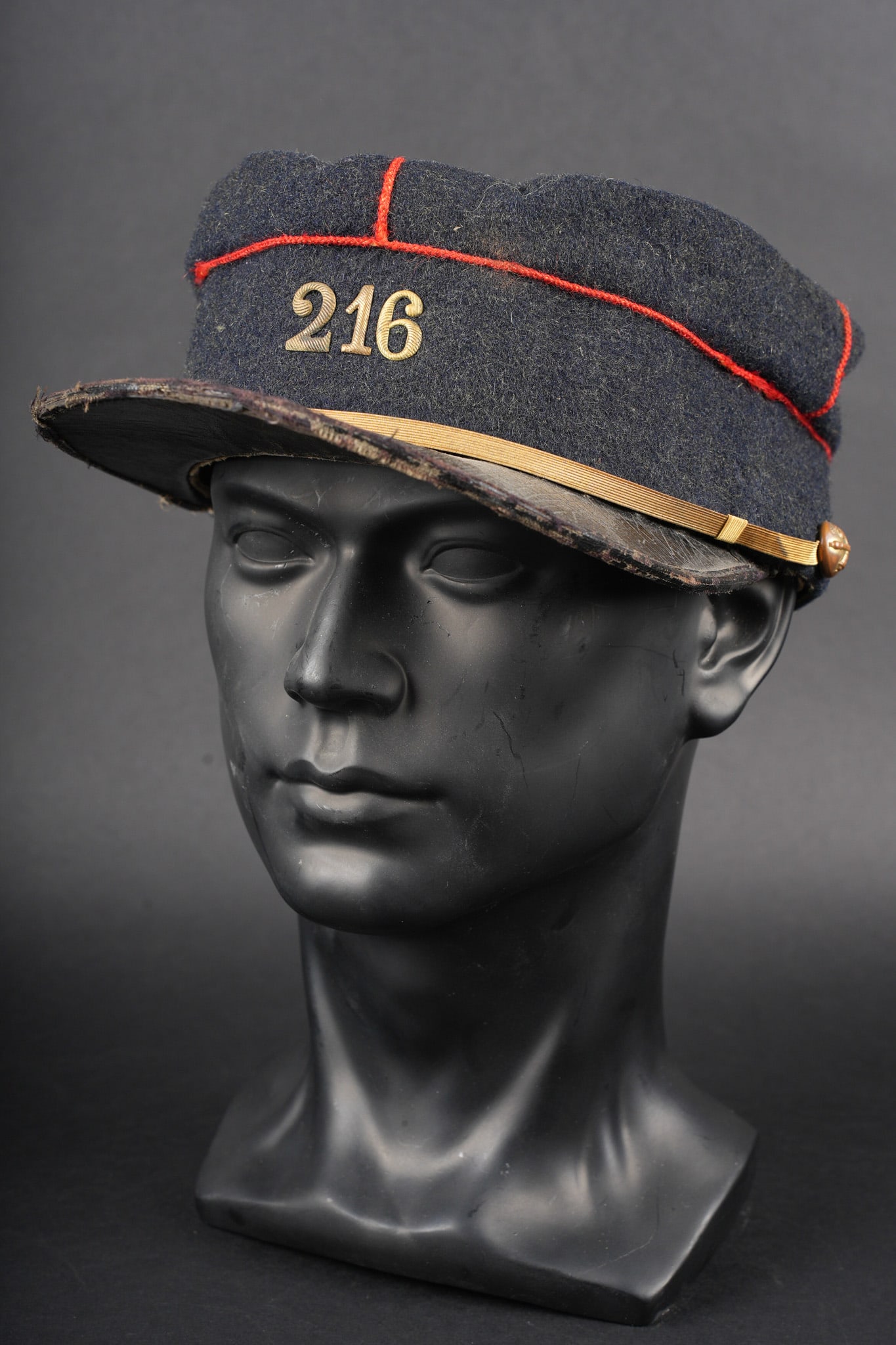 Kepi 216eme d artillerie. Kepi, 216th Artillery Regiment: Kepi 216eme d artillerie. En drap bleu fonce, passepoil ecarlate, chiffre 216 en metal rapporte, regiment de reserve du 16eme d artillerie de Clermont Ferrand. Fausse jugulaire plate doree retenue
