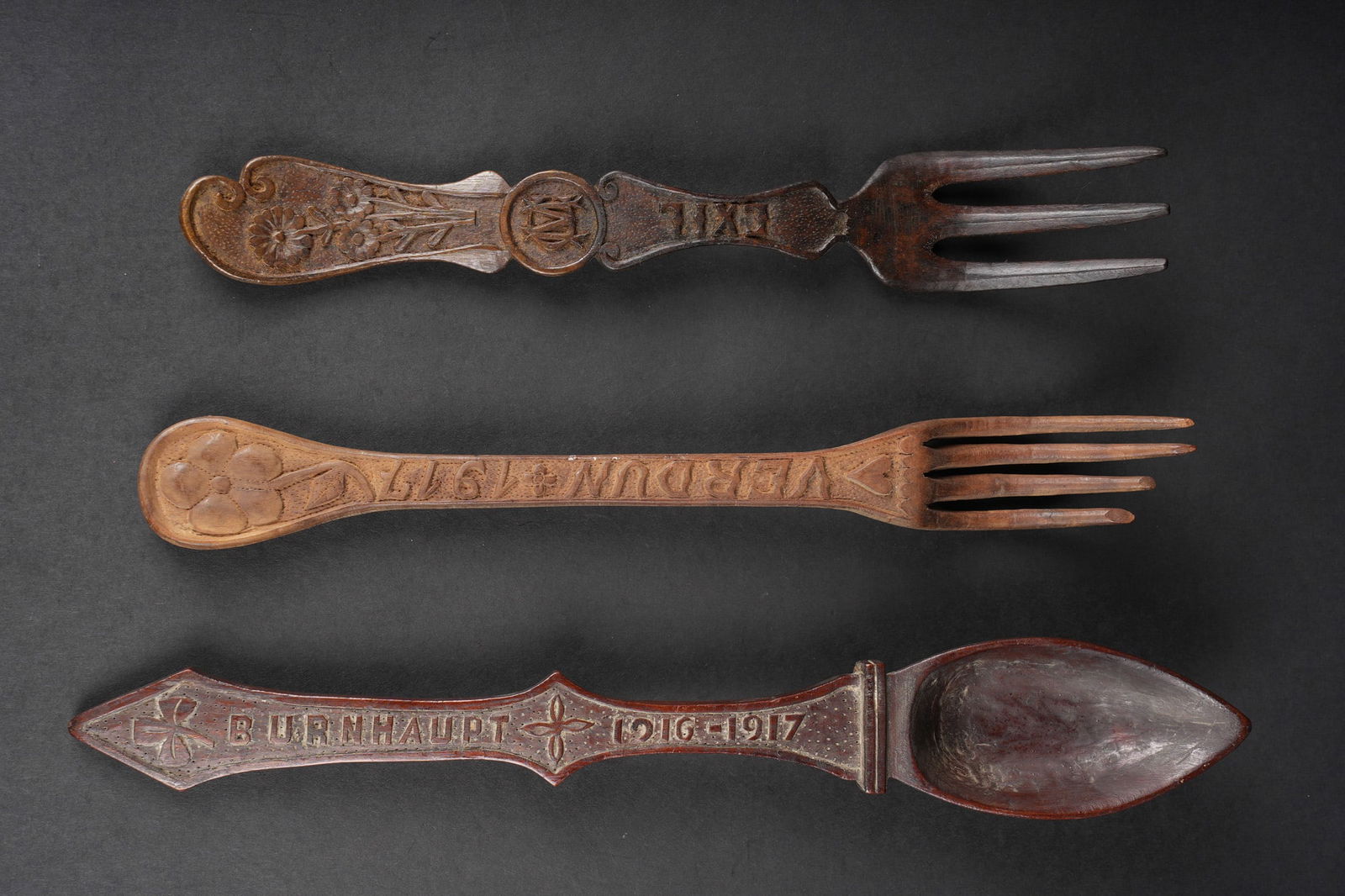 Lots de couverts artisanat de tranchees. Lot of trench-art cutlery: Lots de couverts artisanat de tranchees. Comprenant une fourchette gravee Verdun 1917, deux dents accidentees. Une fourchette gravee Exil ainsi que les initiales CM et un decor florale. Une cuillere