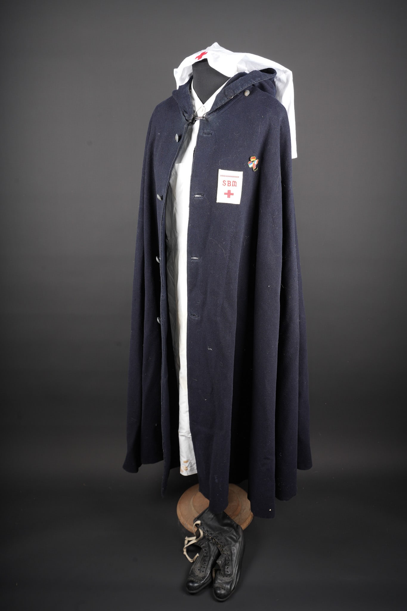 Lot d infirmiere. Nurse’s lot: Ensemble d infirmiere. Comprenant une cape en drap bleu fonce se fermant par quatre boutons portant la mention Societe Secours aux blesses. Sur la poitrine gauche est cousu l insigne de secours aux