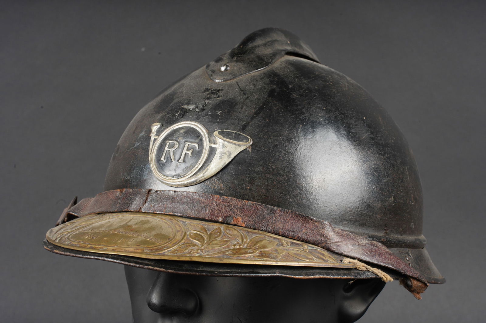 Casque Adrian 1915 chasseurs. Adrian helmet, Model 1915, Chasseurs: Casque Adrian 1915 chasseurs. Casque modele 1915 en peinture bleu horizon d usine recouverte d une peinture noire. Attribut modele 1915 les chasseurs dont le cor de chasse et les lettres RF ont ete re